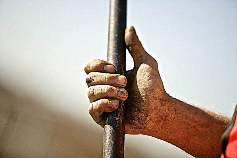 A close up photo of a workers dirty soiled hands holding a bar with shallow depth of field and selective focus. Workers Hand Holding a Bar