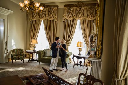 Wide photo of a middle age loving couple inside a large beautiful, plantation style home, being affectionate and holding drinks in nice light. Shot for the Mississippi Tourism campaign for advertising, branding, collateral and broadcast motion assets. Environmental portrait, and we are a industrial photographer, on location photographer & location commercial photographer. VisitMS Couple Large Plantation Living Room