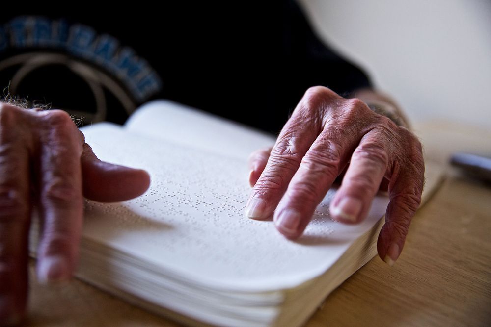 The hands of a blind man, on a book reading Braille. Senior citizen reading, tight shot of his hands and book of Braille only. Selective focus. Photographed for a United Way advertising campaign. I am a advertising photographer, on location photographer & location commercial photographer. Photo of one of the many people that the United Way is assisting. Shallow depth of field. Man Reading Braille, Hands Only