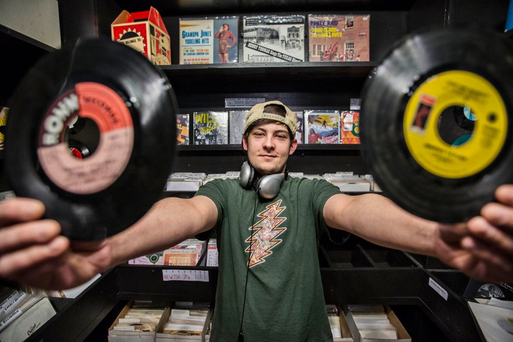 Portrait of millennial male holding up two vinyl records, with a cocky expression looking into the camera, in Oxford, MS. Shot for the Mississippi Tourism campaign for advertising, branding, collateral and broadcast motion assets. Environmental portrait, and we are a industrial photographer, on location photographer & location commercial photographer. VisitMS Millennial Male Holding Vinyl Records