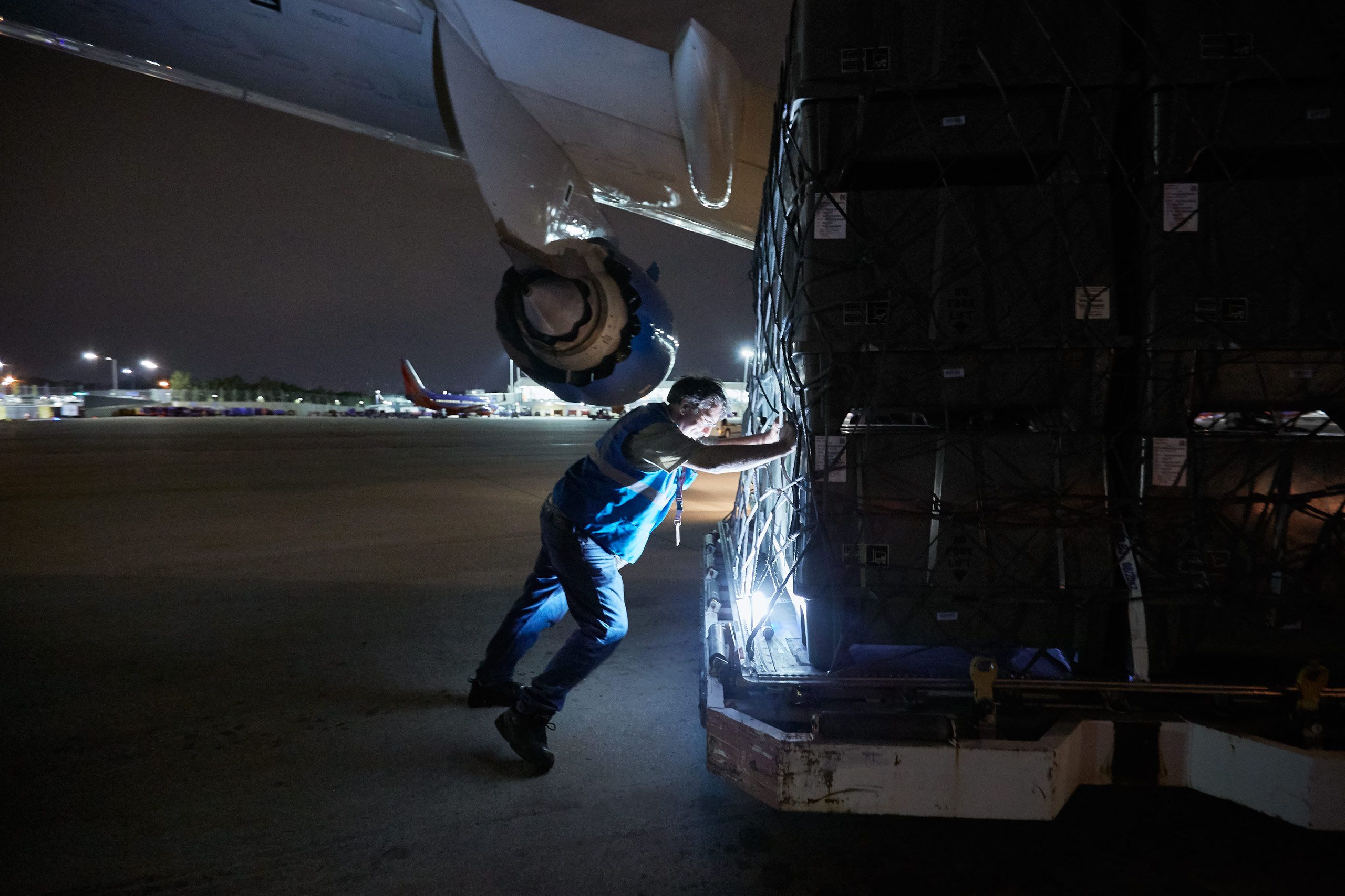 Worker Pushing Cargo Toward a 747 Cargo Transportation Plane
