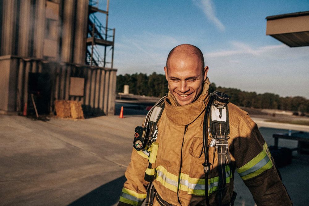 Photo of Loss Control person smiling after a long day of training. He is dressed in protective fire gear, and ready for action and to respond and mitigate a disaster as it relates to risk management in the insurance industry. Environmental portrait, and we are a industrial photographer, on location photographer & location commercial photographer. Fireman After a Long Day of Training