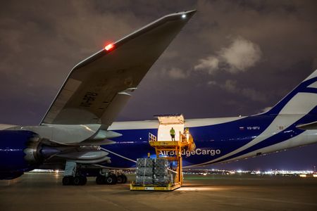 Wide side view of a Boeing 747-8 Freighter at an airport, with the left side cargo door open with a worker, Load Master standing at the edge, silhouetted. The plane is being unloaded and then being re loaded with cargo at night time. Next stop, the other side of the world! A project shooting for the air cargo industry. This project was amazing as an industrial photographer, on location photographer & location commercial photographer. Man Standing In Open Cargo Door of 747 Airplane