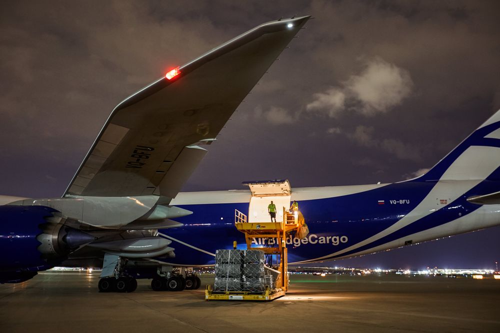 Wide side view of a Boeing 747-8 Freighter at an airport, with the left side cargo door open with a worker, Load Master standing at the edge, silhouetted. The plane is being unloaded and then being re loaded with cargo at night time. Next stop, the other side of the world! A project shooting for the air cargo industry. This project was amazing as an industrial photographer, on location photographer & location commercial photographer. Man Standing In Open Cargo Door of 747 Airplane