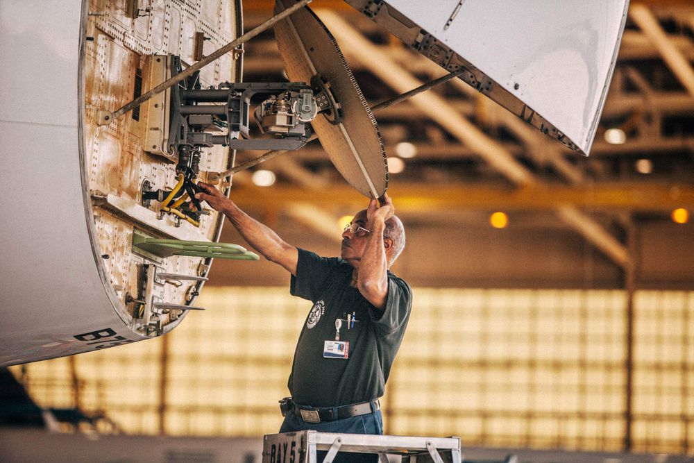 A mechanic is working on the nose of an airplane and has it lifted open exposing the radar system inside of it. Mechanic Working on an Airplane