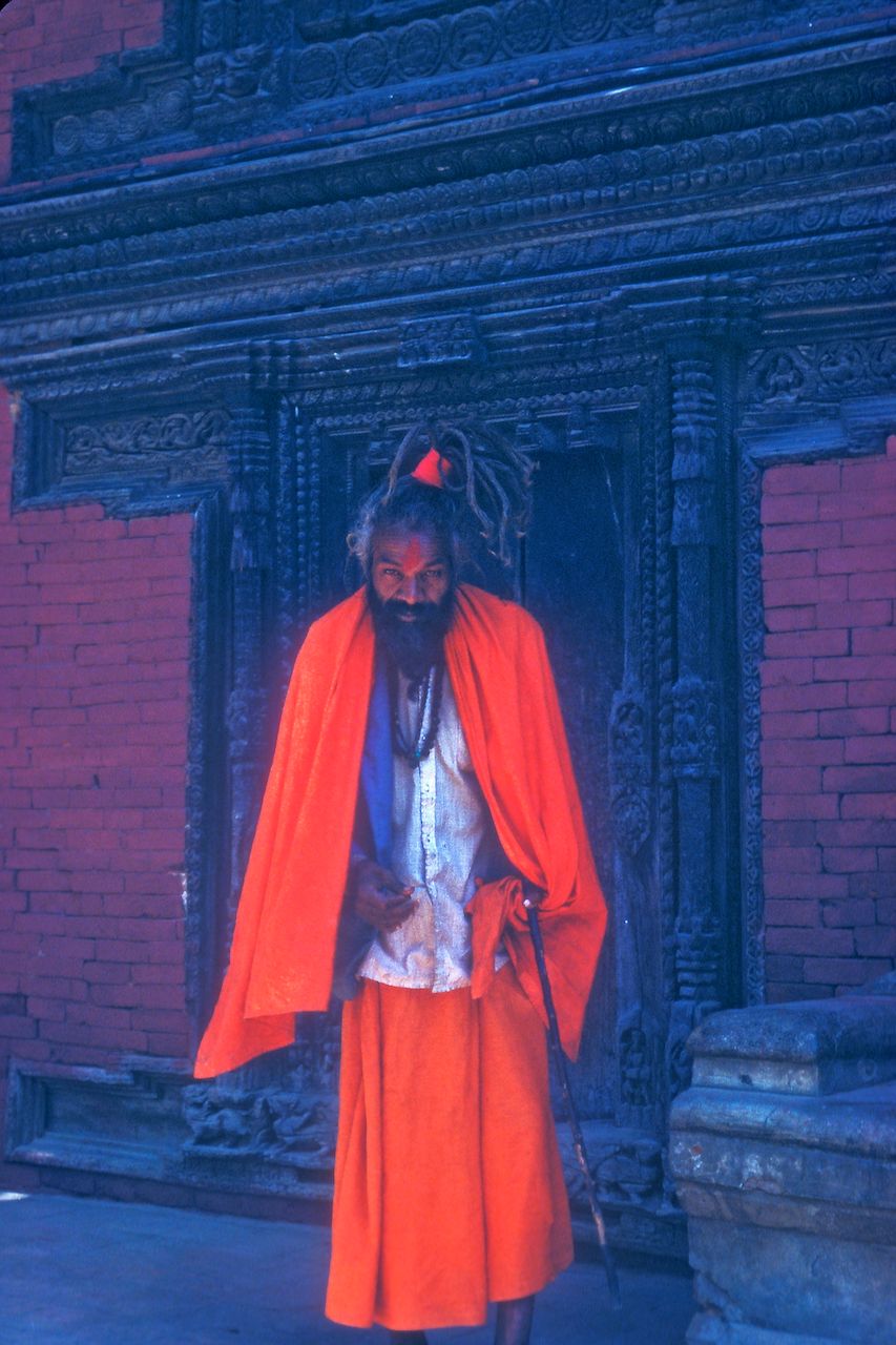 Begging outside a temple. Patan, Nepal. Orange robed shaman.