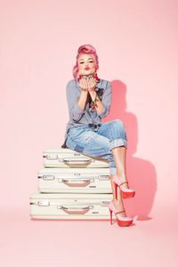 photo of Influencer and make up artist Kandee Johnson with oversized retro suitcases on pink background