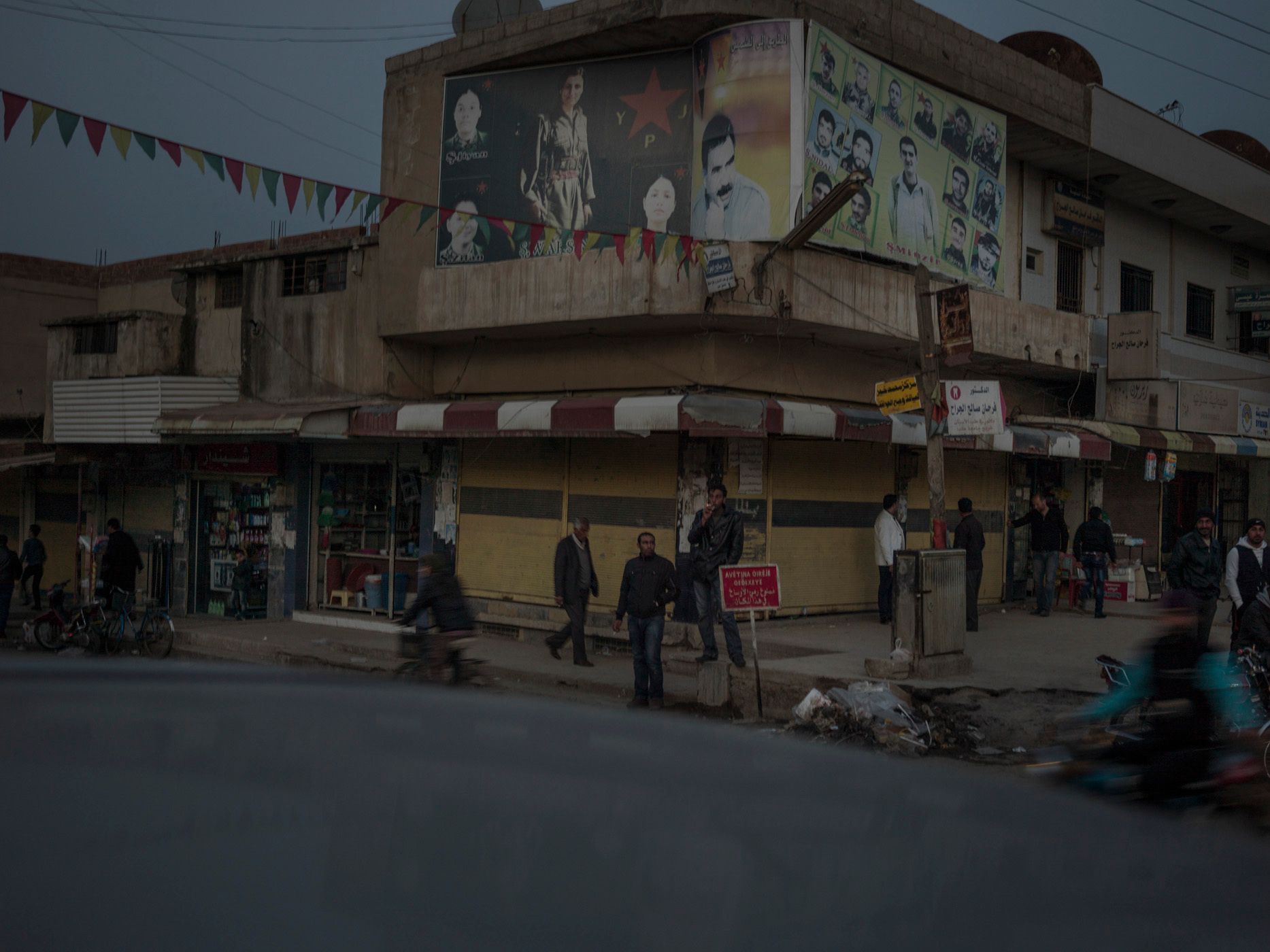 People in the local market of Terbespe, passing by a moral wall-painting with embedded pictures of female martyrs of YPJ next to the portrait of Abdullah Ocalan. The words above Ocalan's image translate as "the path towards the sun". 18.jpg