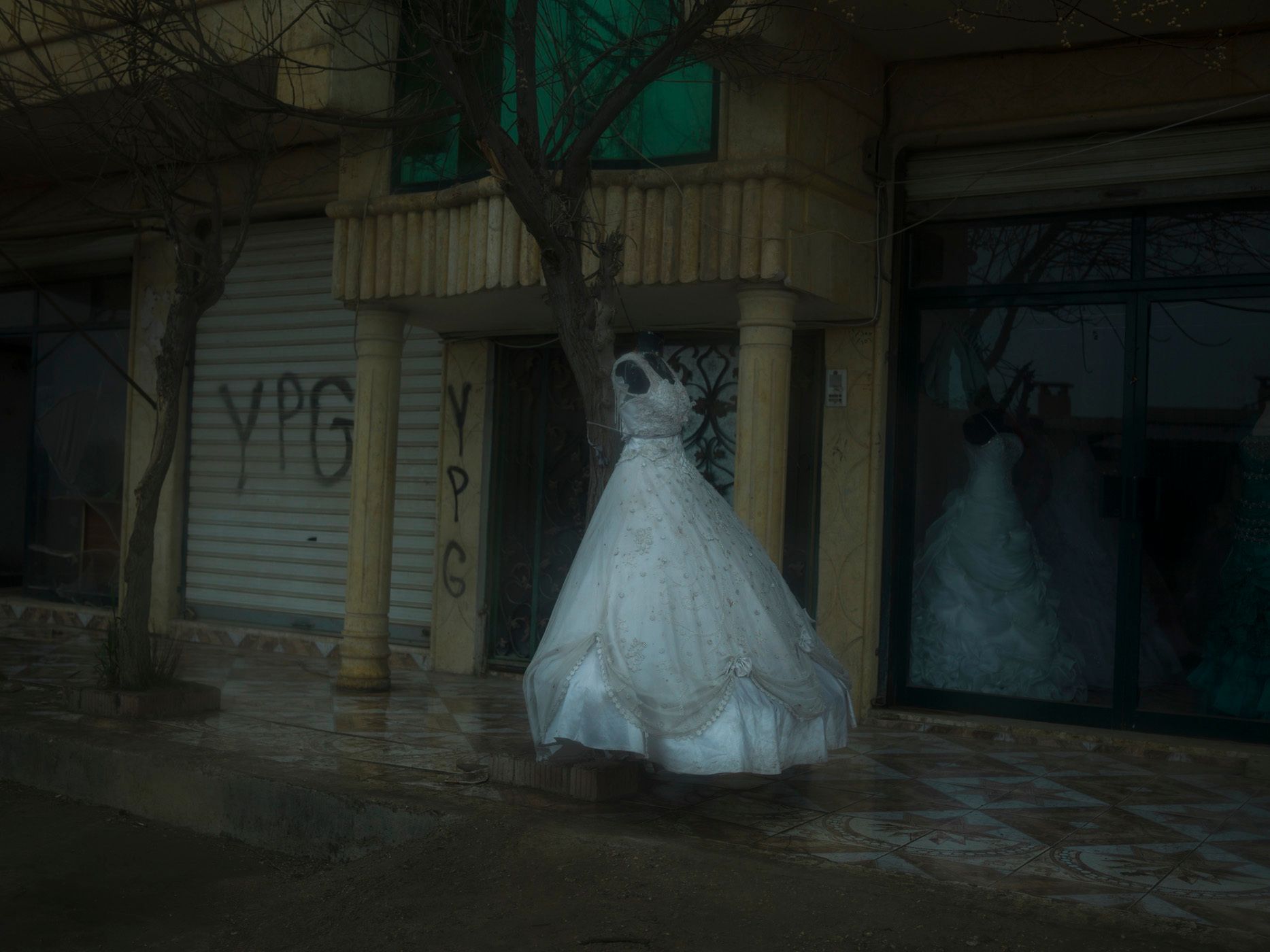 A wedding dress placed outside a bridal shop in a town near Qamishlou. YPG graffiti can be seen on the walls of adjacent buildings.YPJ and YPG members are neither allowed to marry nor can they have sexual relationships. Their ideology suggests that they are already married to their country and beliefs. Ocalan believes that the source of capitalism is the foundation of family. 19.jpg