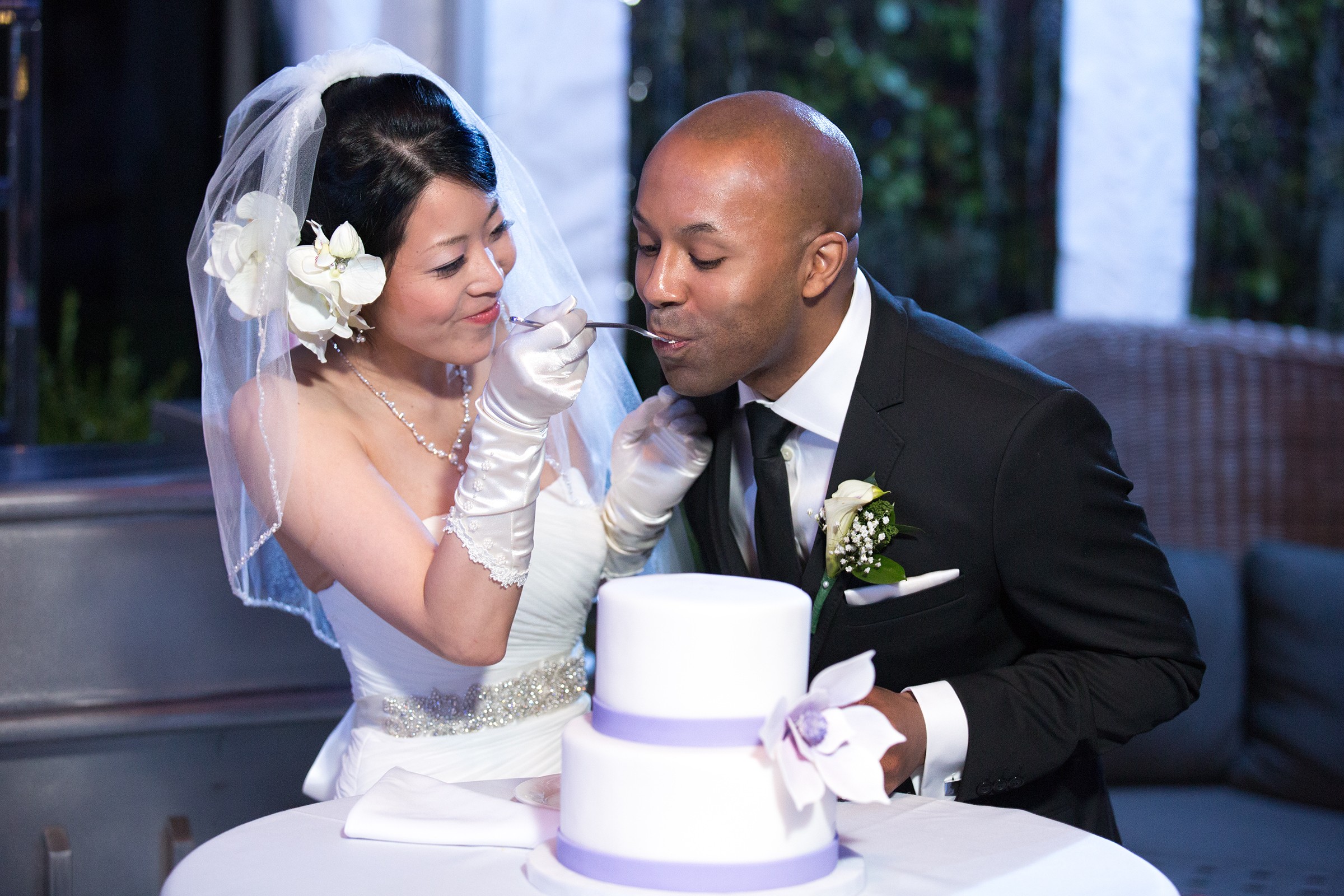 Bride feeding groom cake in violet‑blue wedding lighting