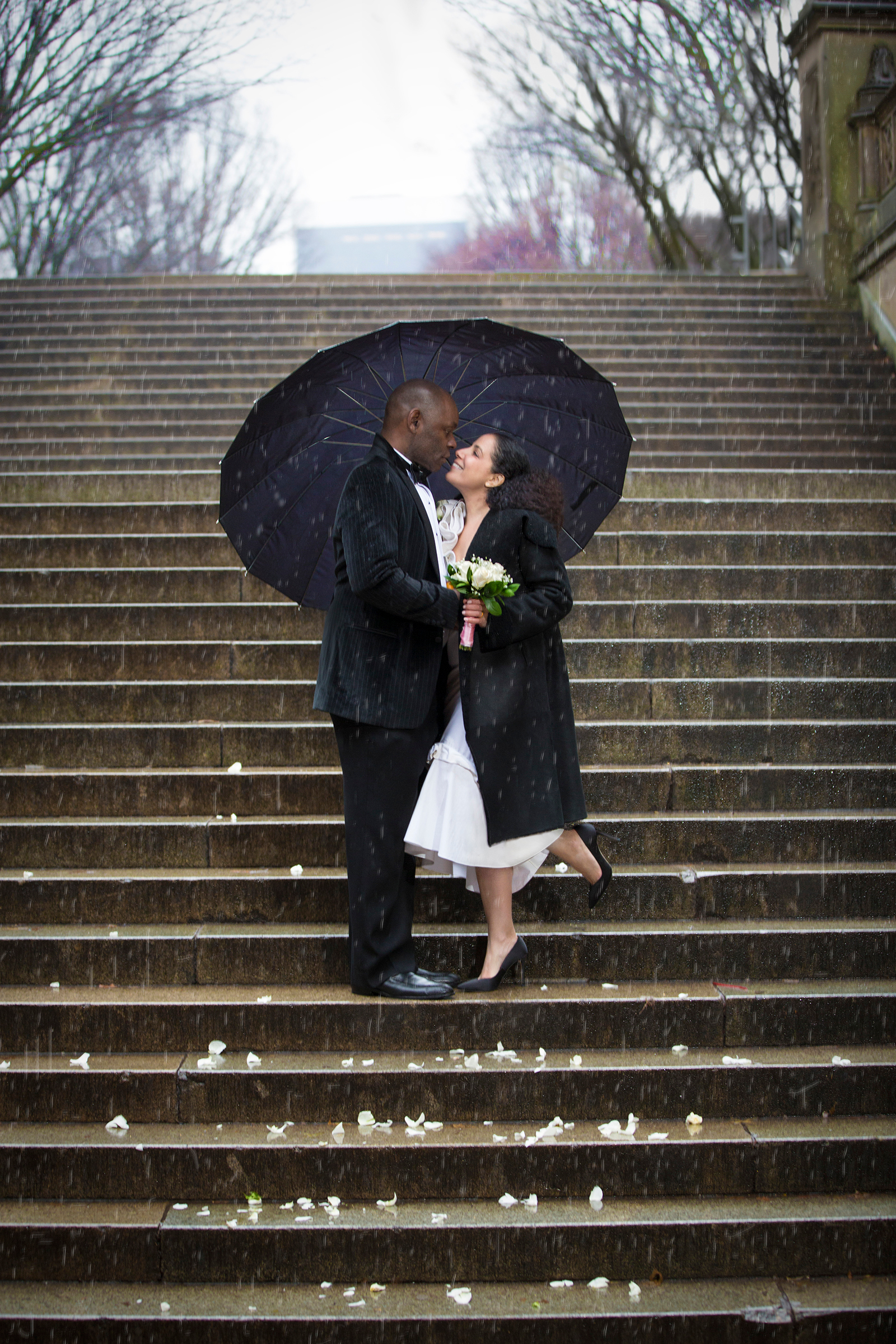 Couple embracing under umbrella on Bethesda Terrace stairs