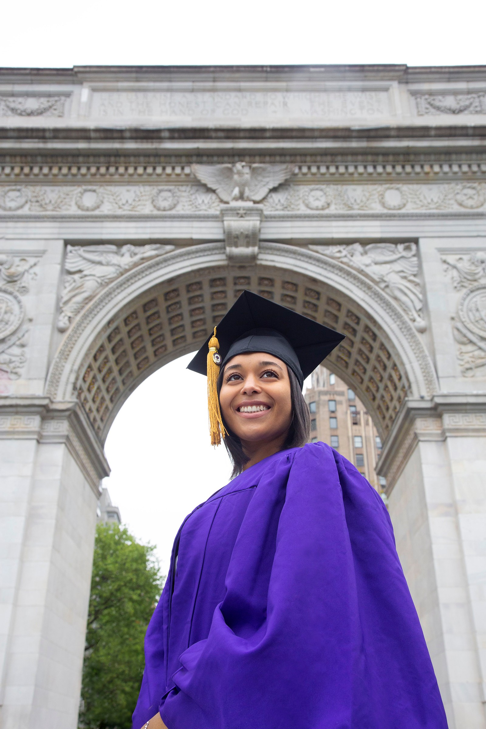 NYU graduate in purple robes under Washington Square Arch