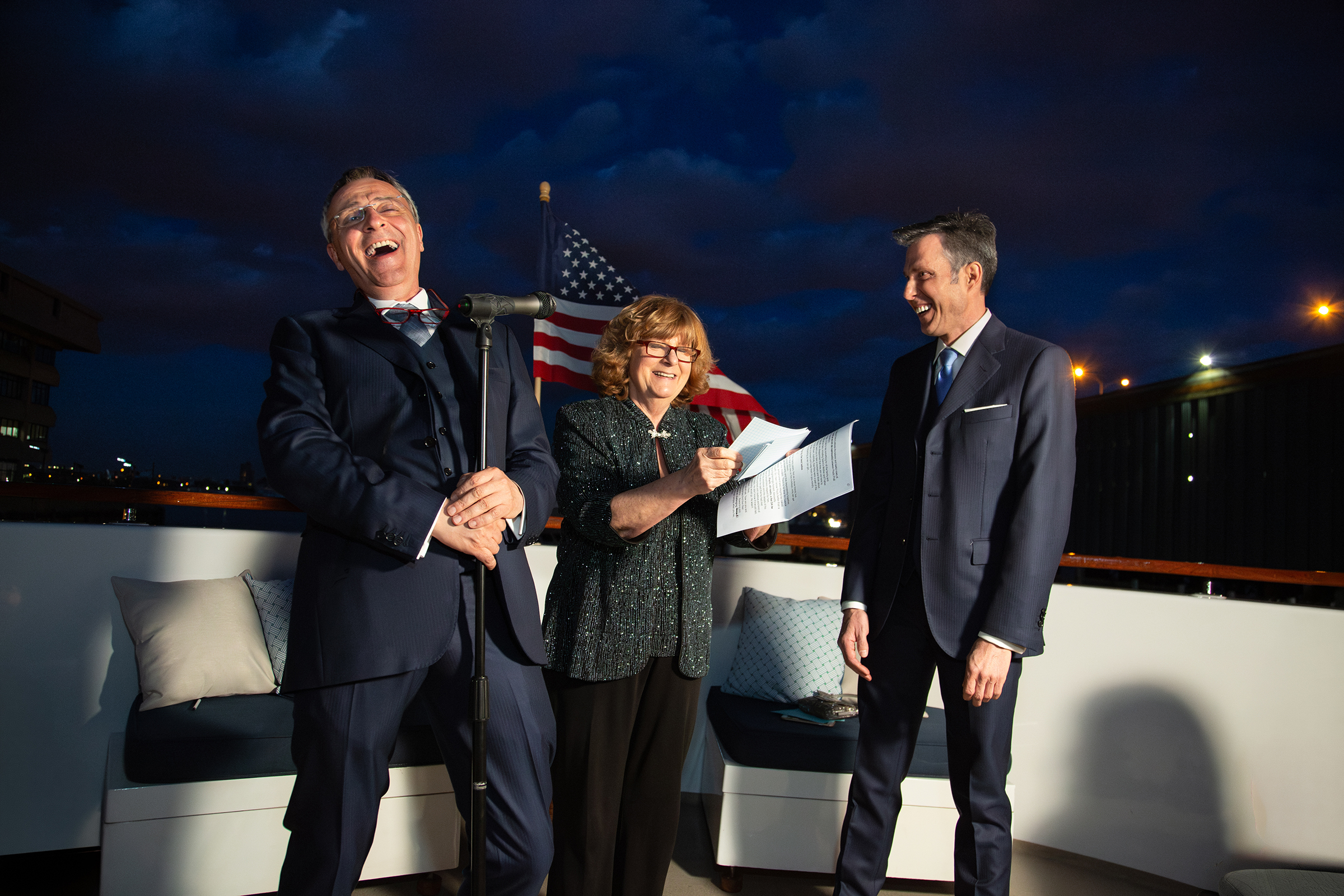 Grooms laughing with officiant during evening yacht wedding