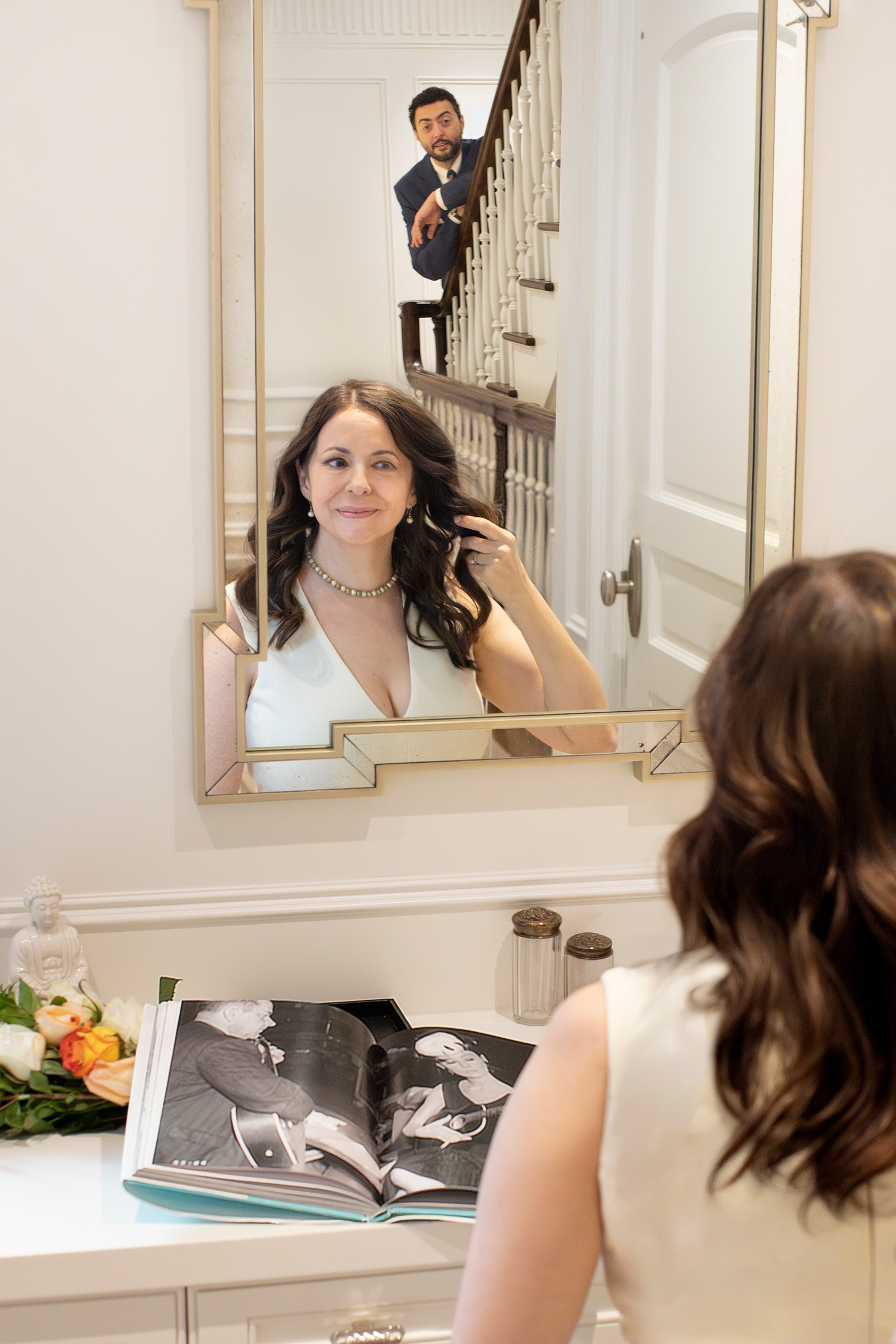 Bride in powder room mirror with groom on staircase behind