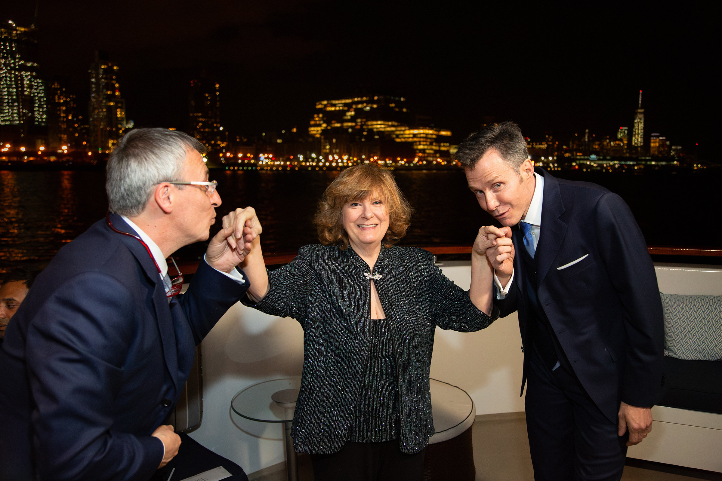 Grooms kissing officiant’s hands aboard yacht with Battery Park lights