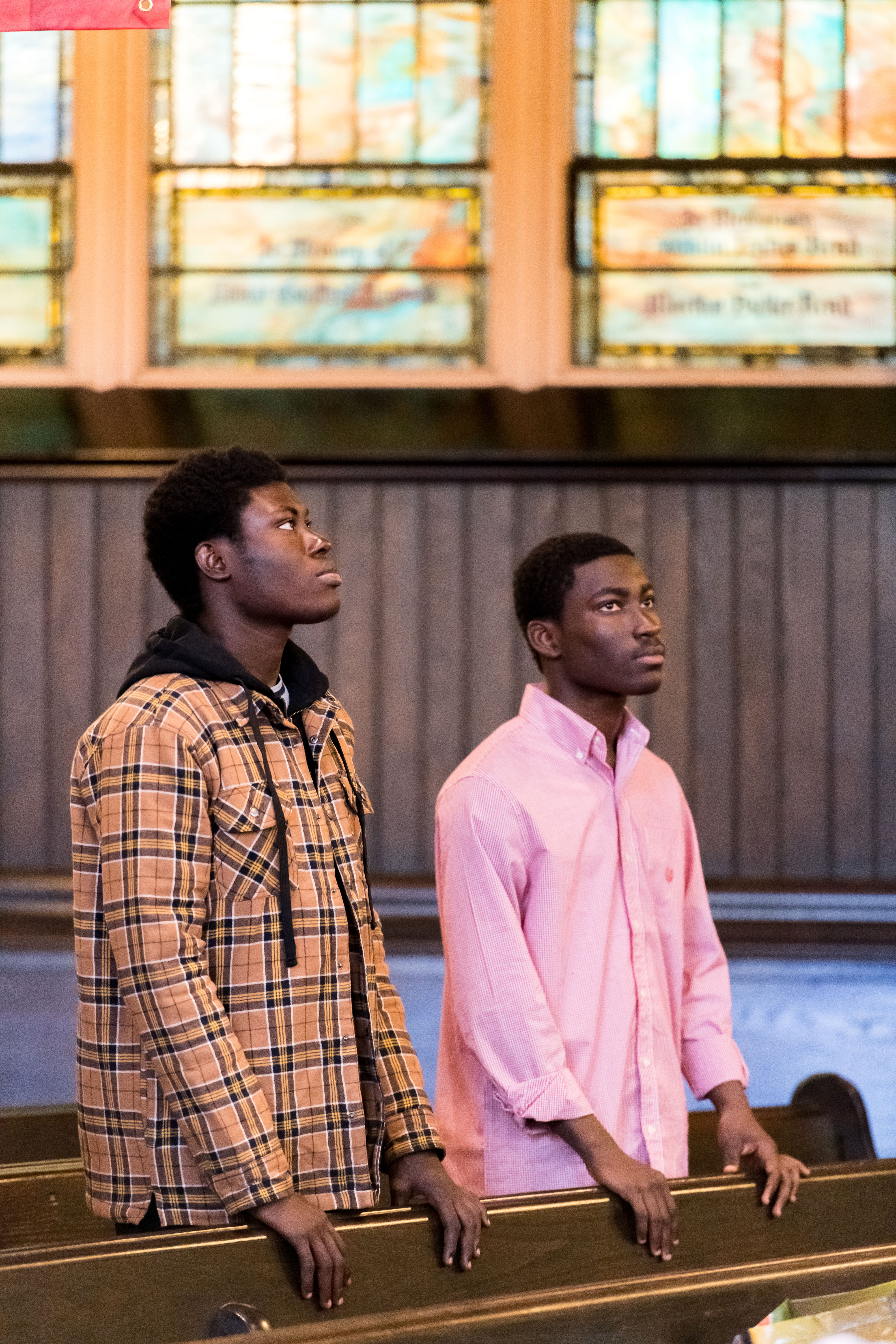 Two young African American men in church with stained glass in background