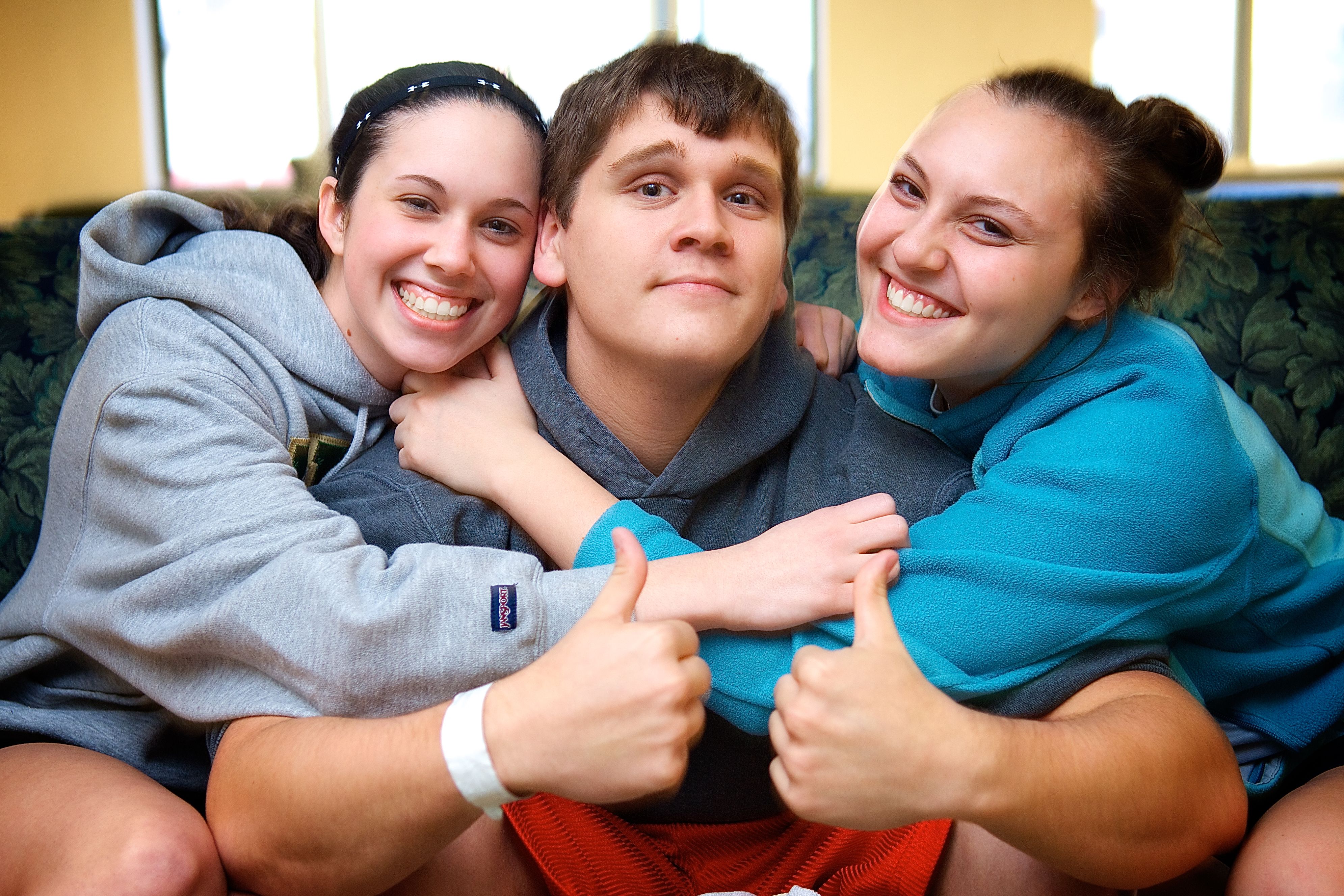 Male college student with twin sisters hugging him gives thumbs up