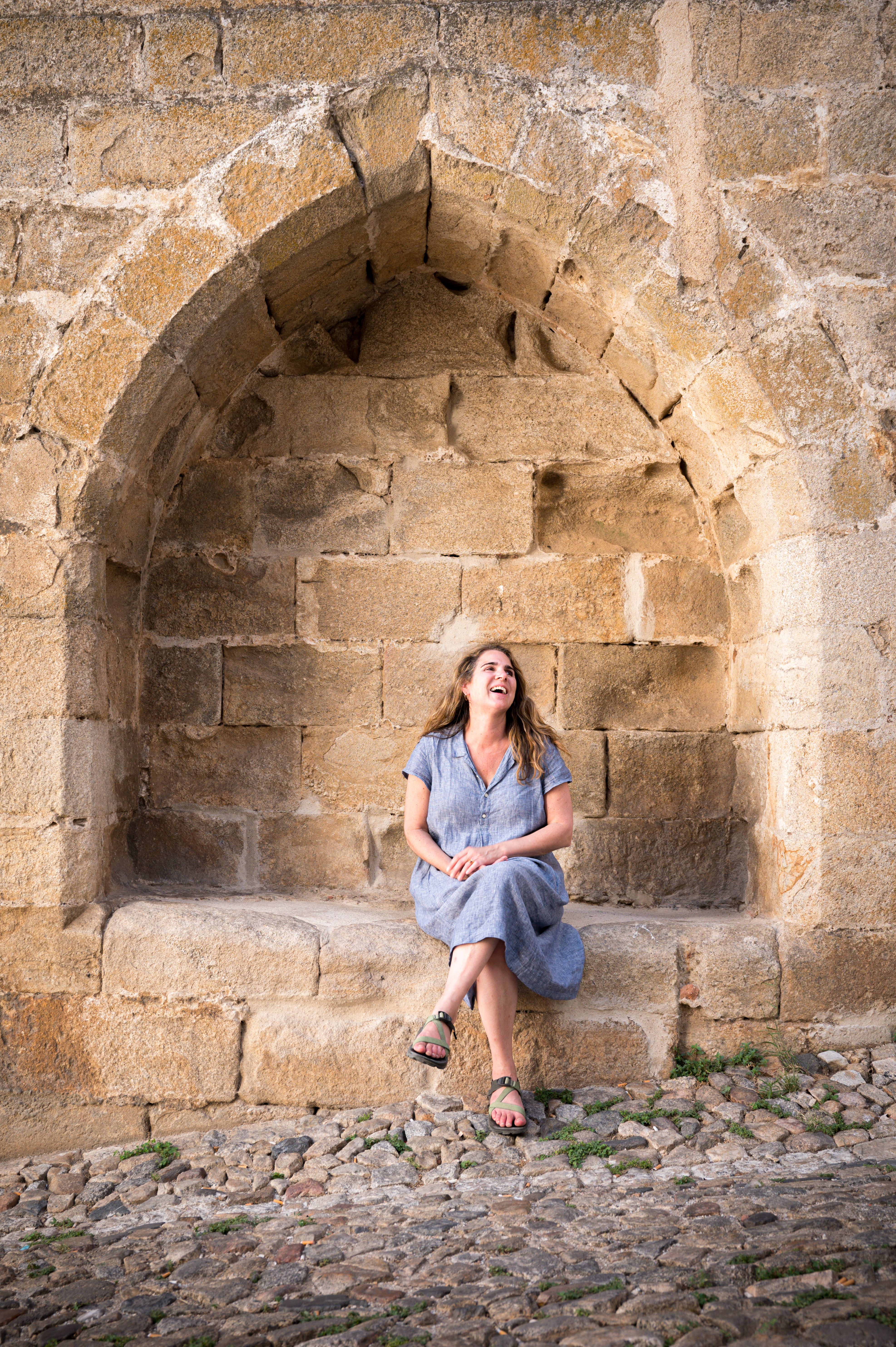 Smiling woman sits in old archway on cobblestone street in Portugal