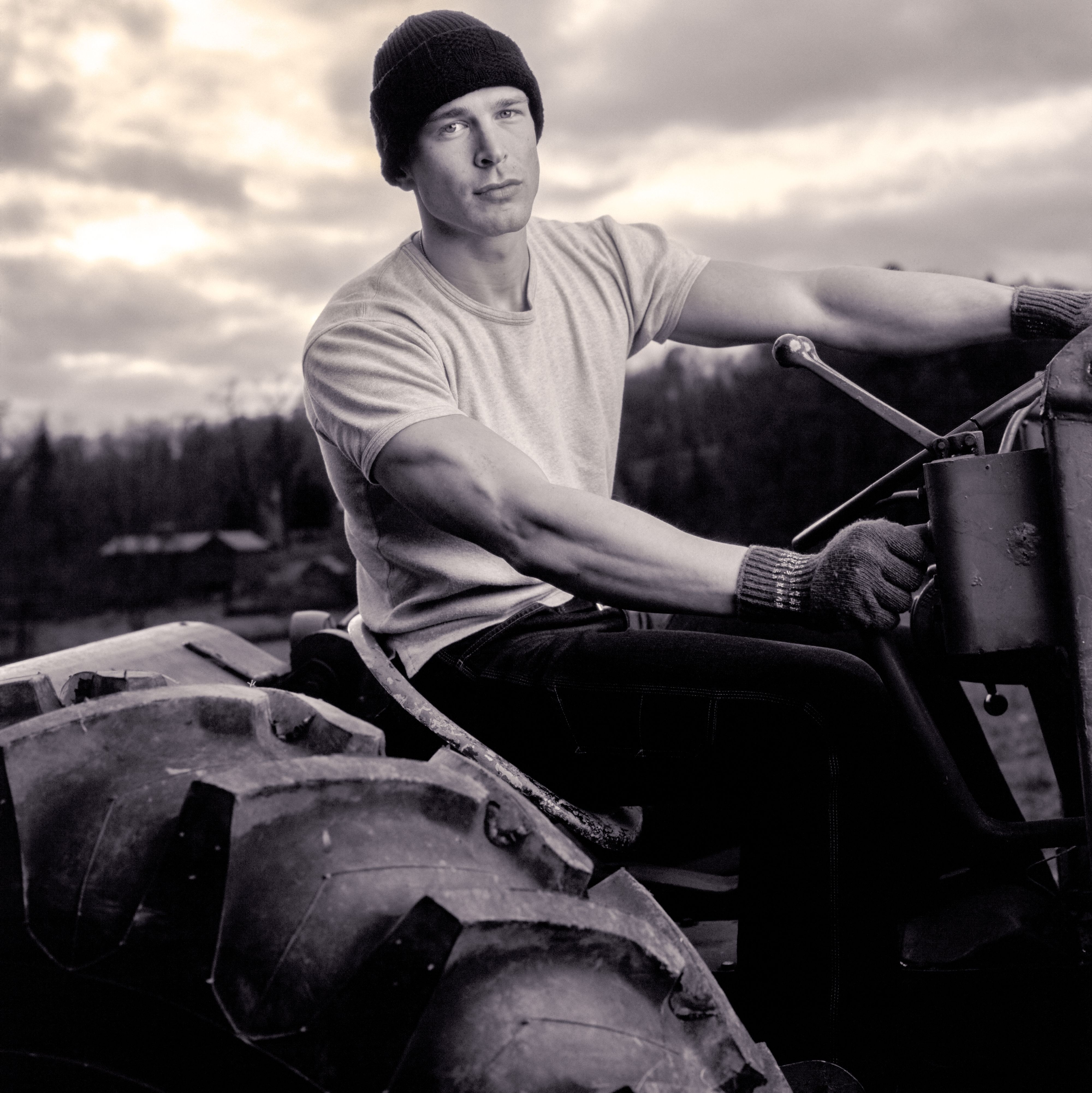 B&W portrait of man wearing hat and t-shirt on tractor