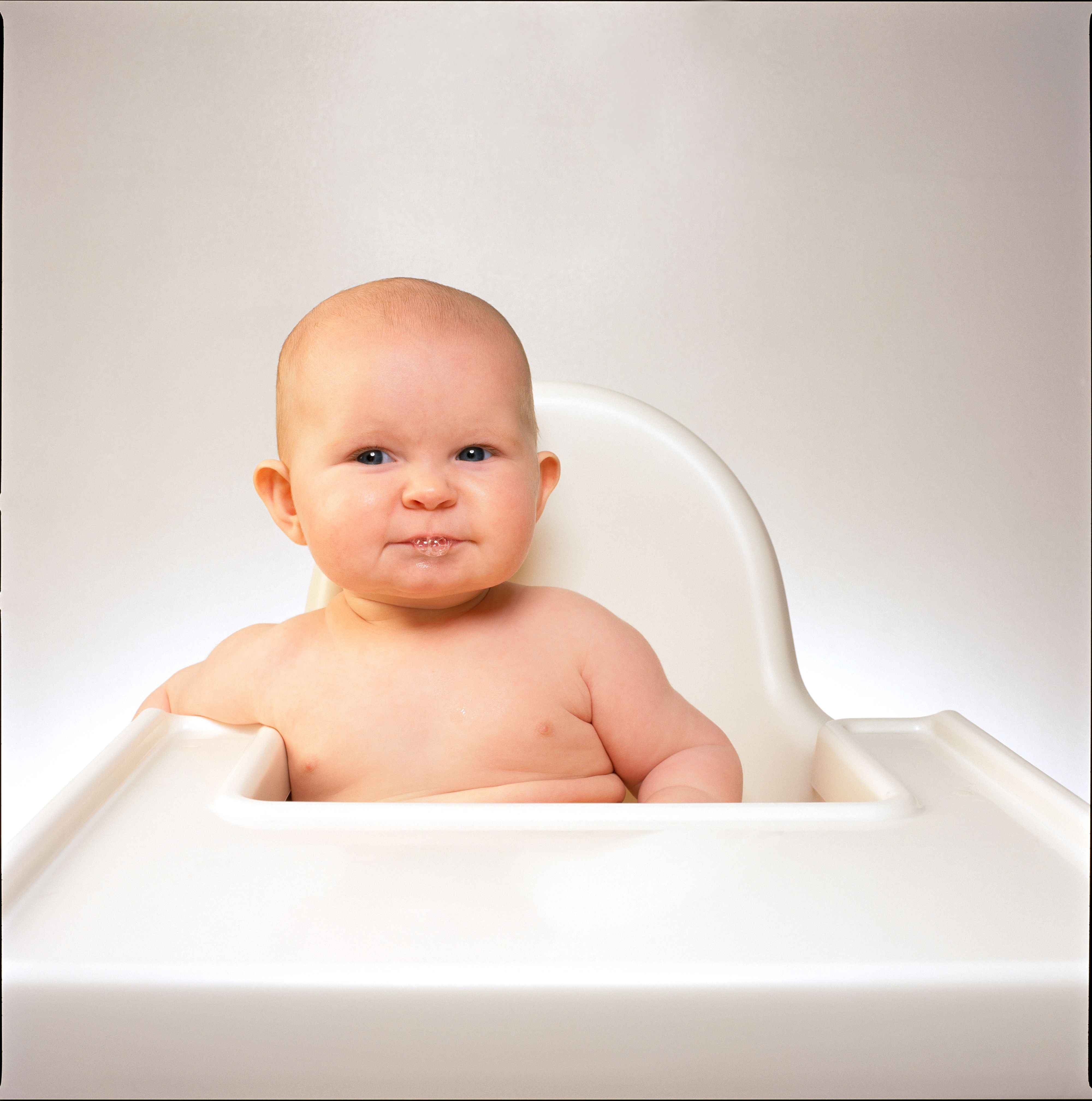 Portrait of baby sitting in white high chair and  blowing bubbles