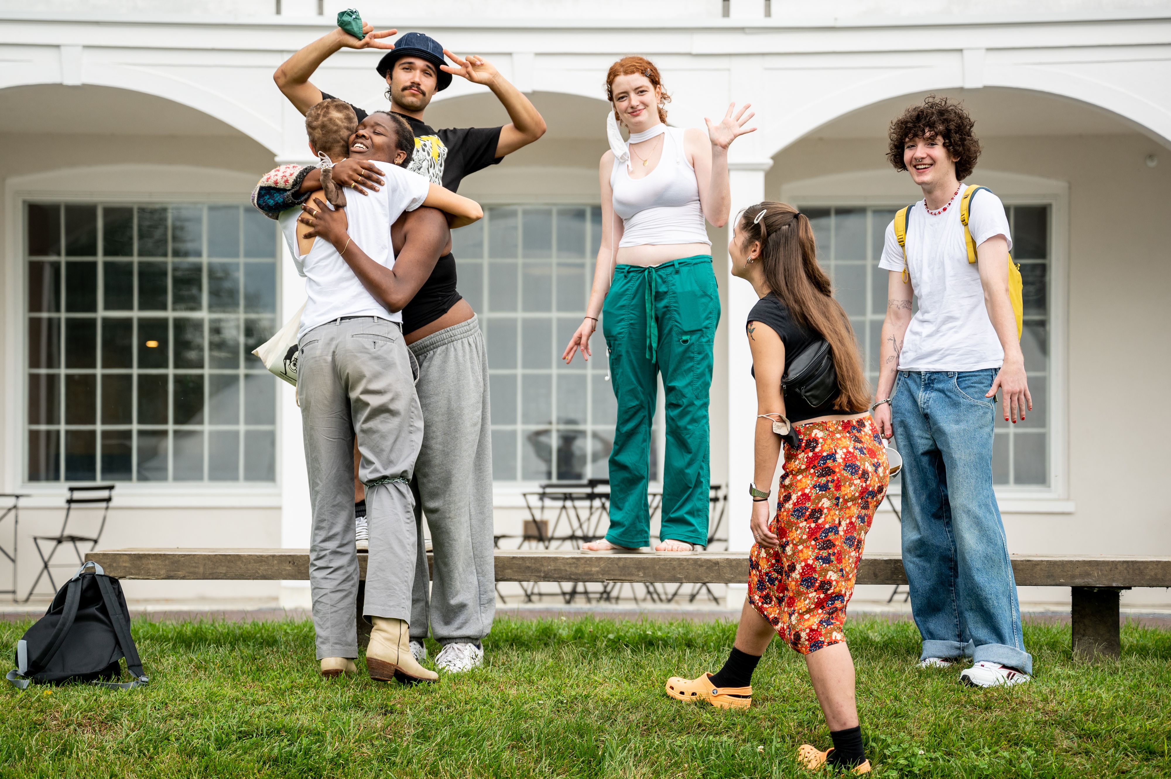 Six college students greet each other outside white building