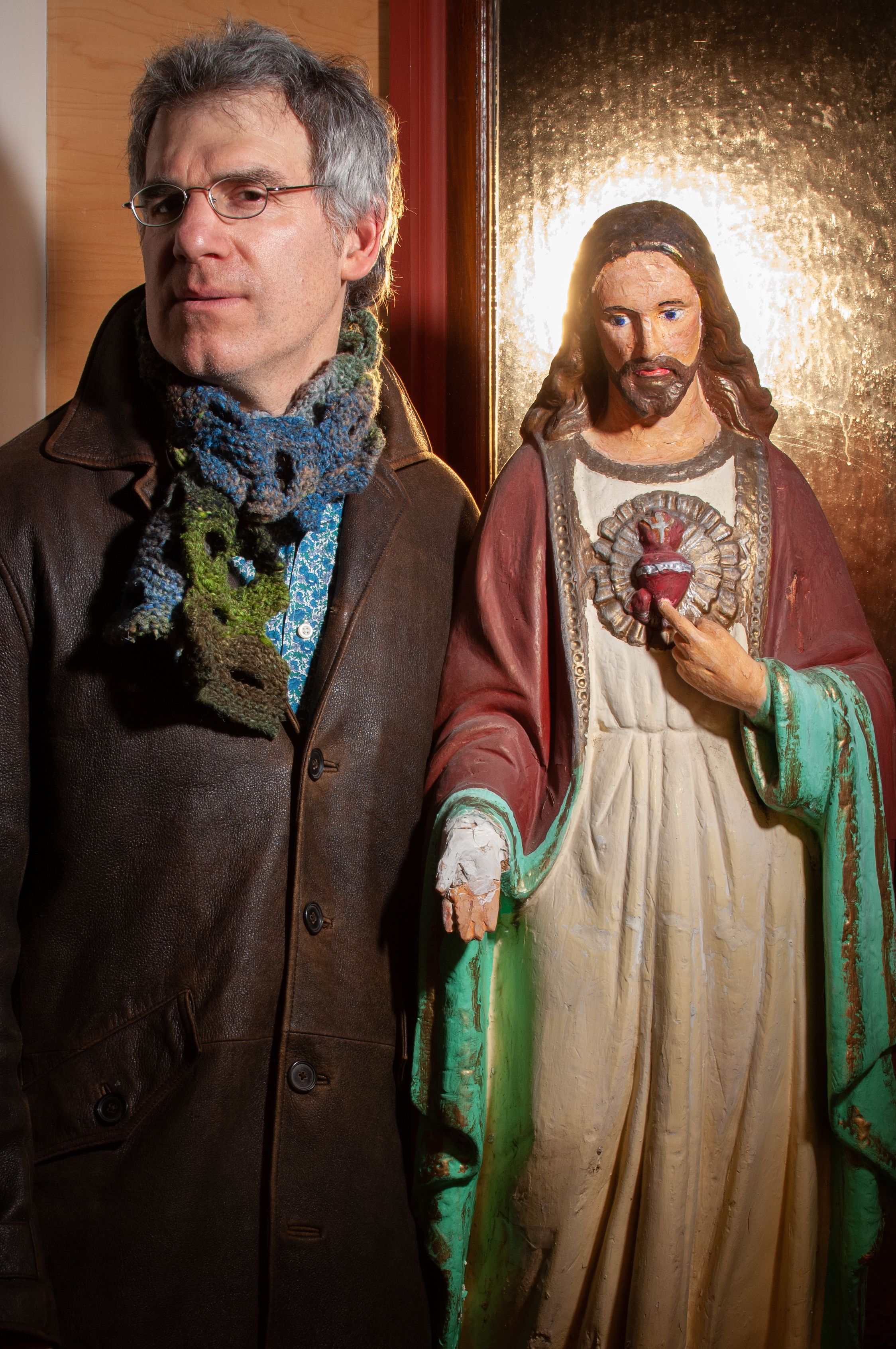 Man in leather jacket and glasses stands next to statue of Jesus
