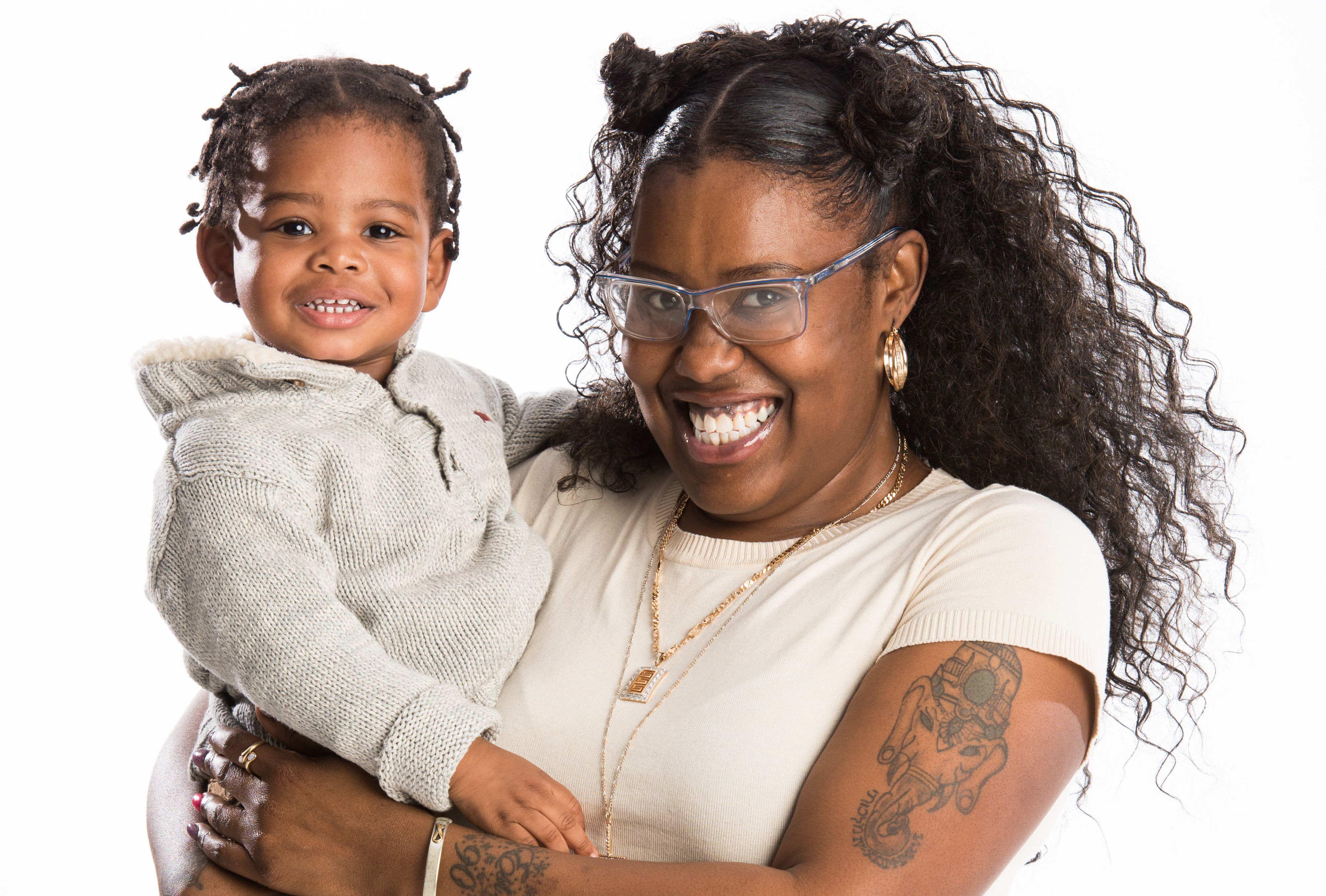 African American woman with glasses and tattoos holds baby in studio portrait
