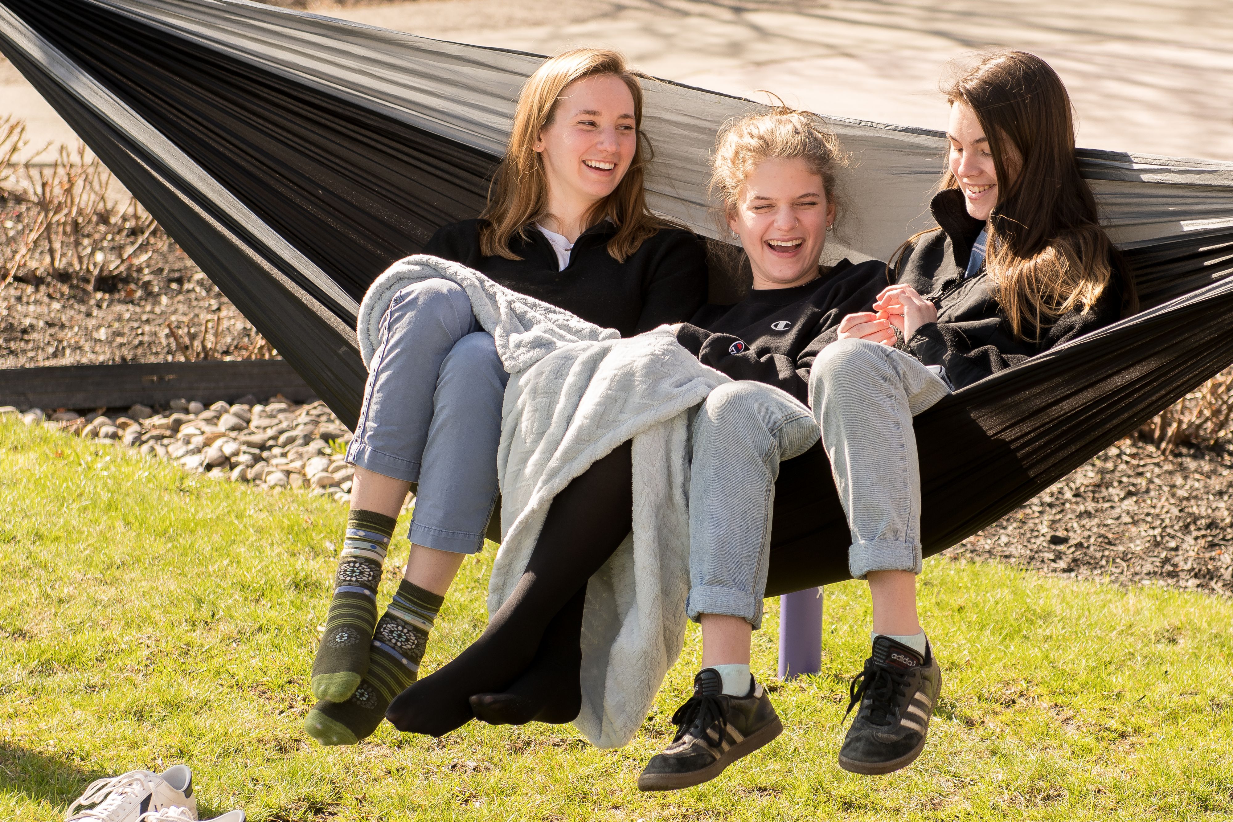 Three female college students laughing together in black hammock