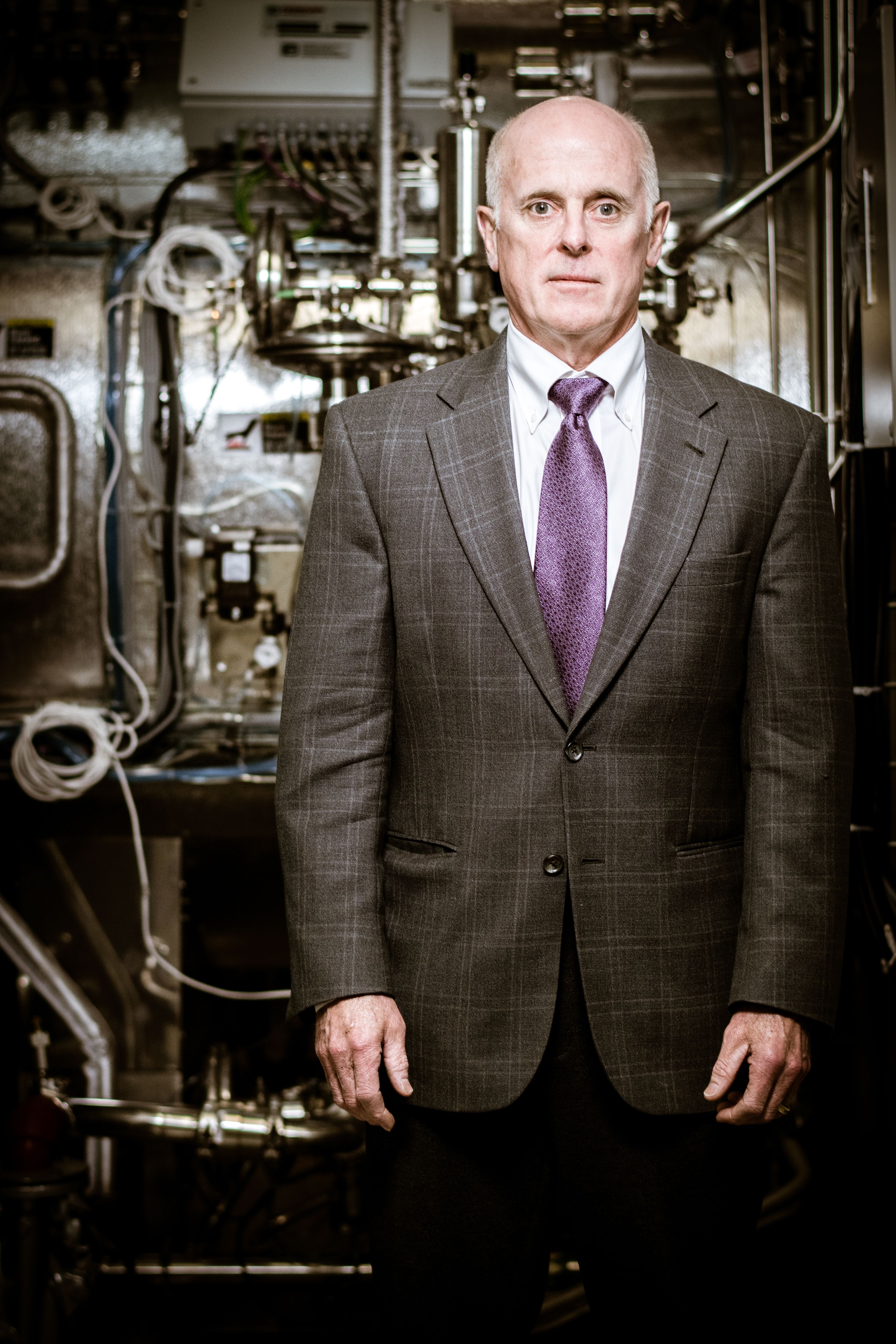 Portrait of male executive in suit with purple tie standing in front of industrial machinery