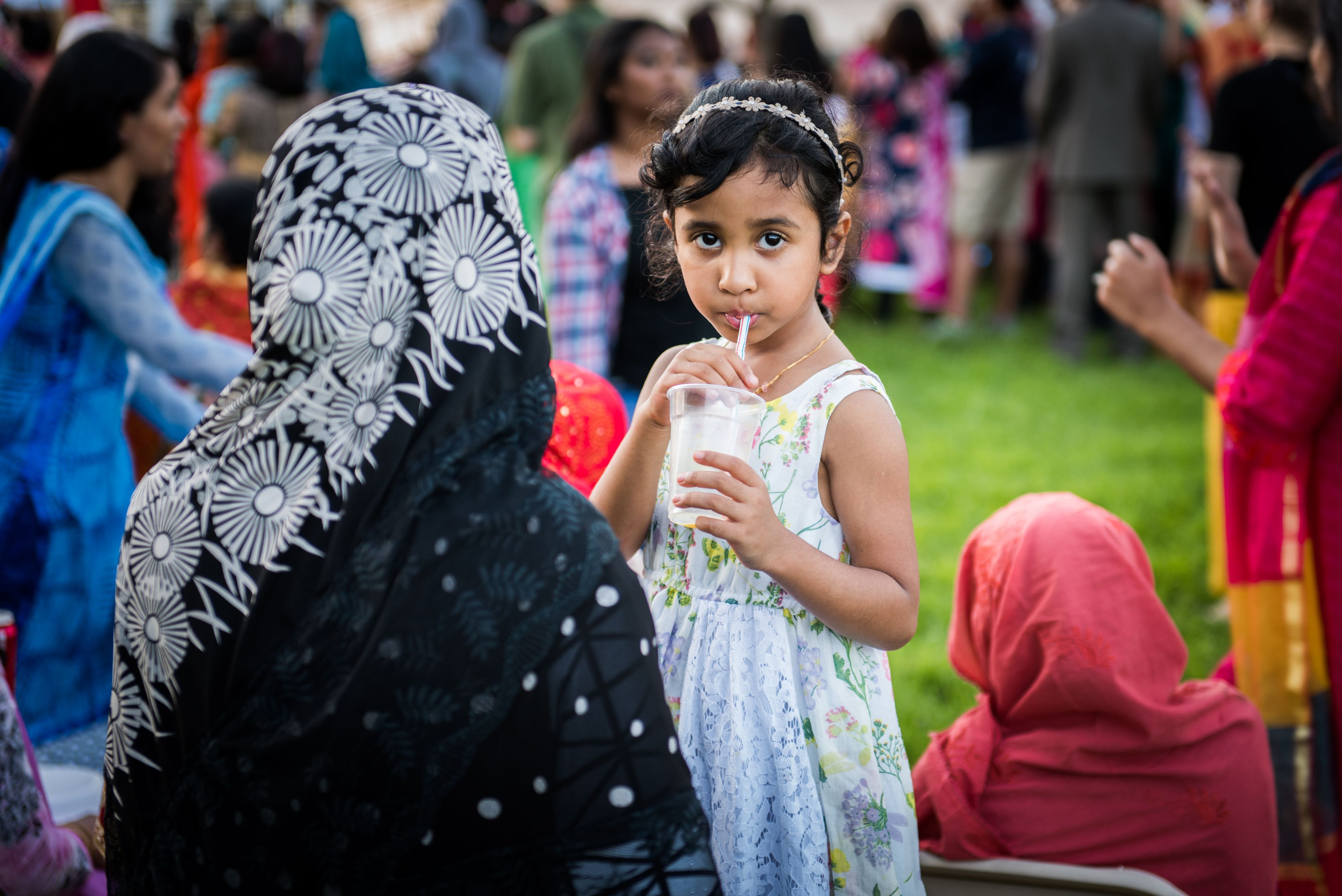 Young middle eastern girl in dress with her mother at outdoor festival having a drink