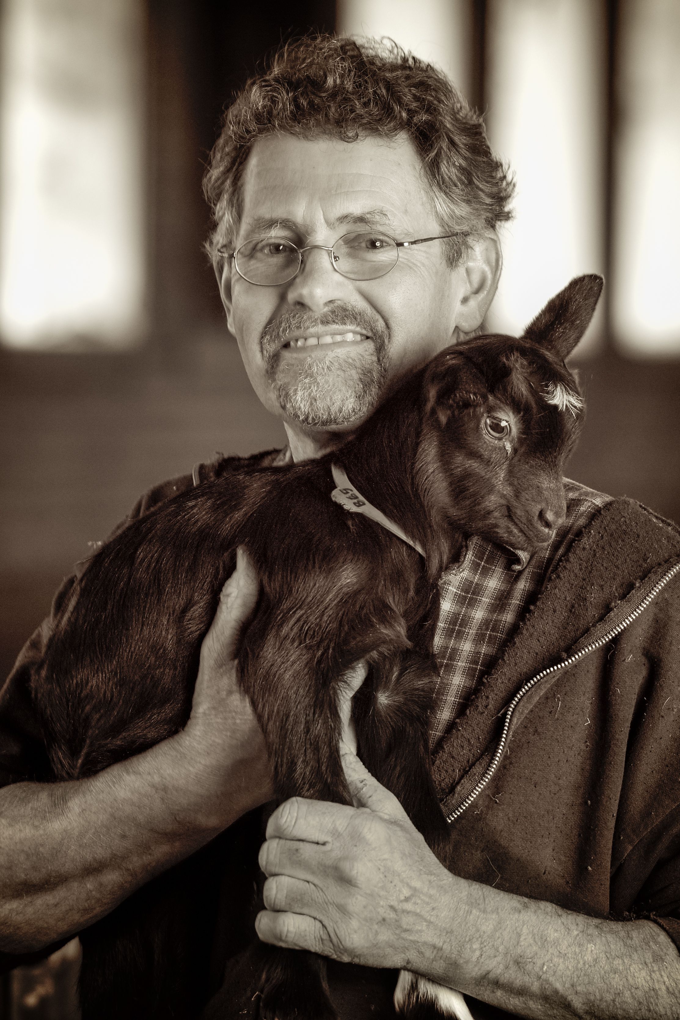 B&W portrait of man in glasses holding baby goat