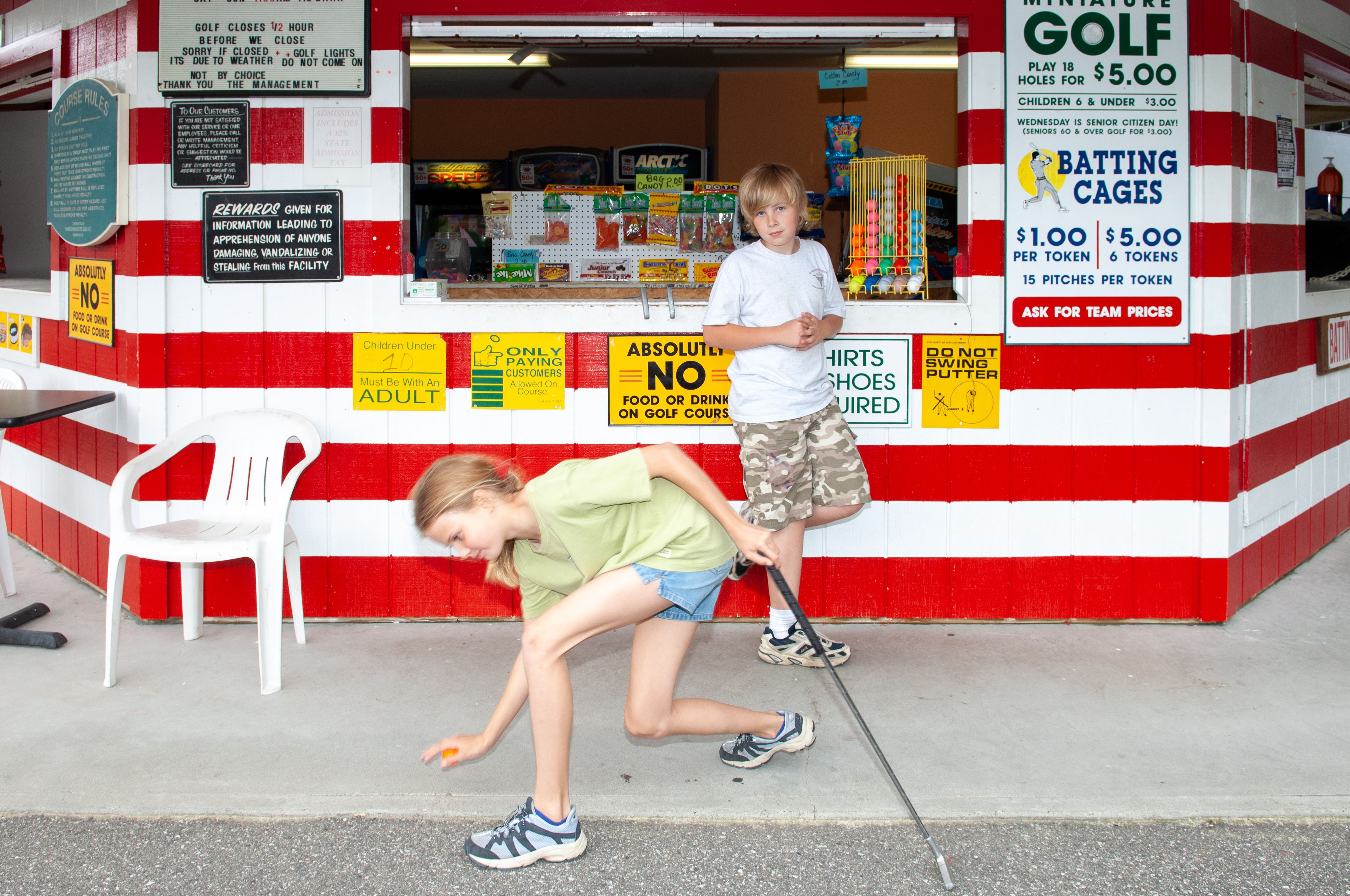 Two kids stand outside red and white striped snack bar at mini golf course