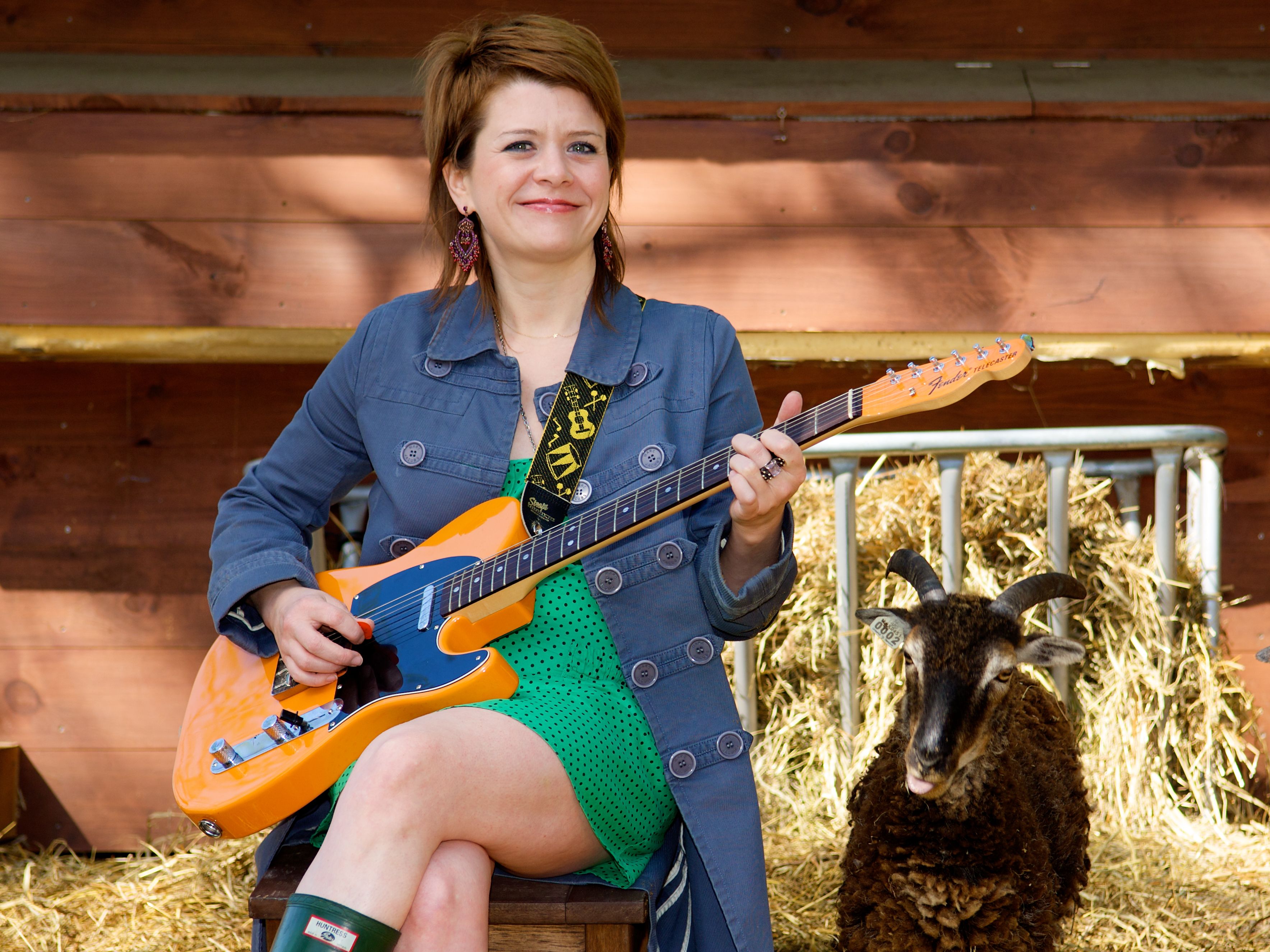 Woman plays orange electric guitar to her goat in outdoor portrait
