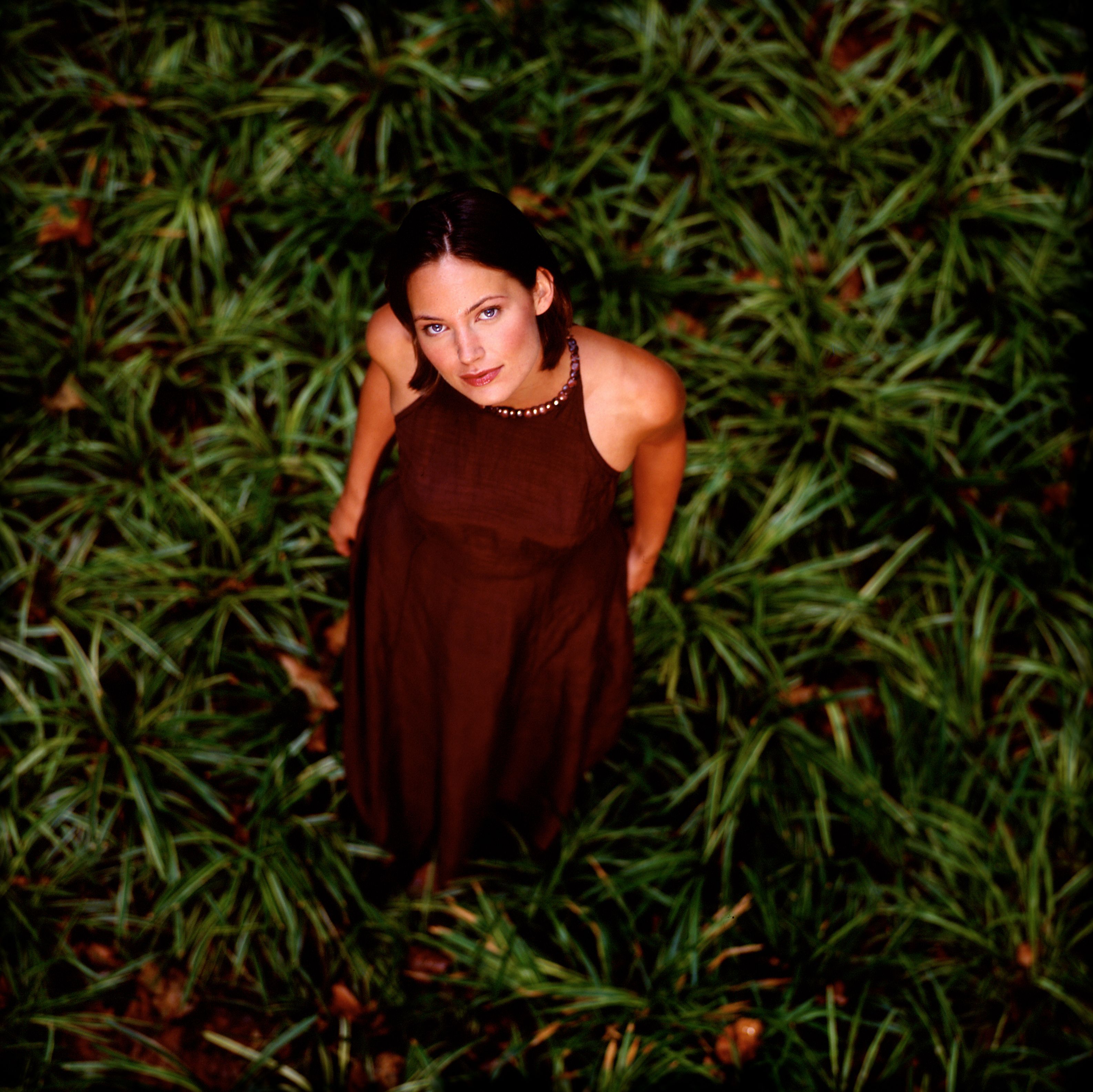 Dark haired model in brown dress stands in grasses along FDR highway in New York City, New York