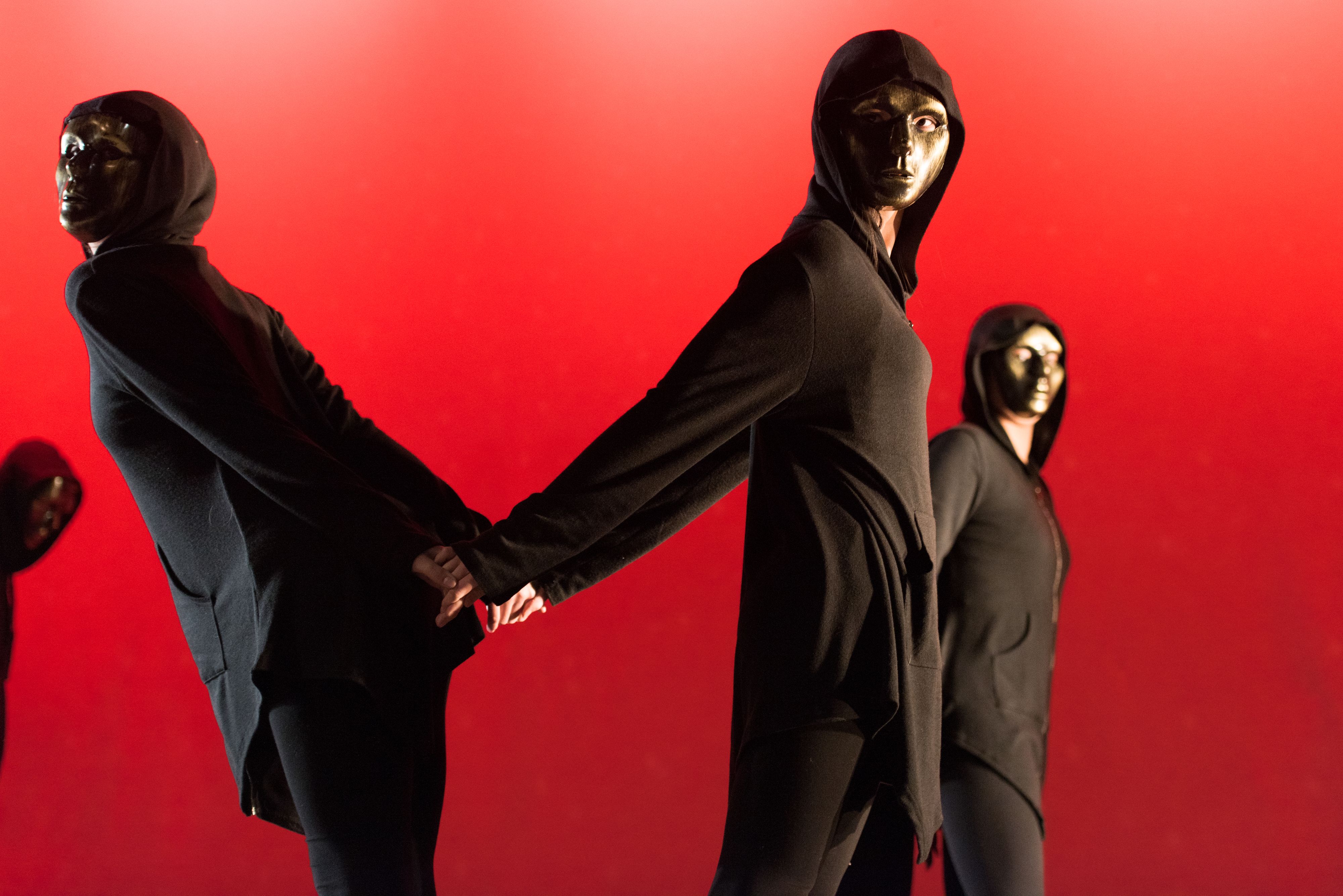 Four dancers in black outfits and masks on red background
