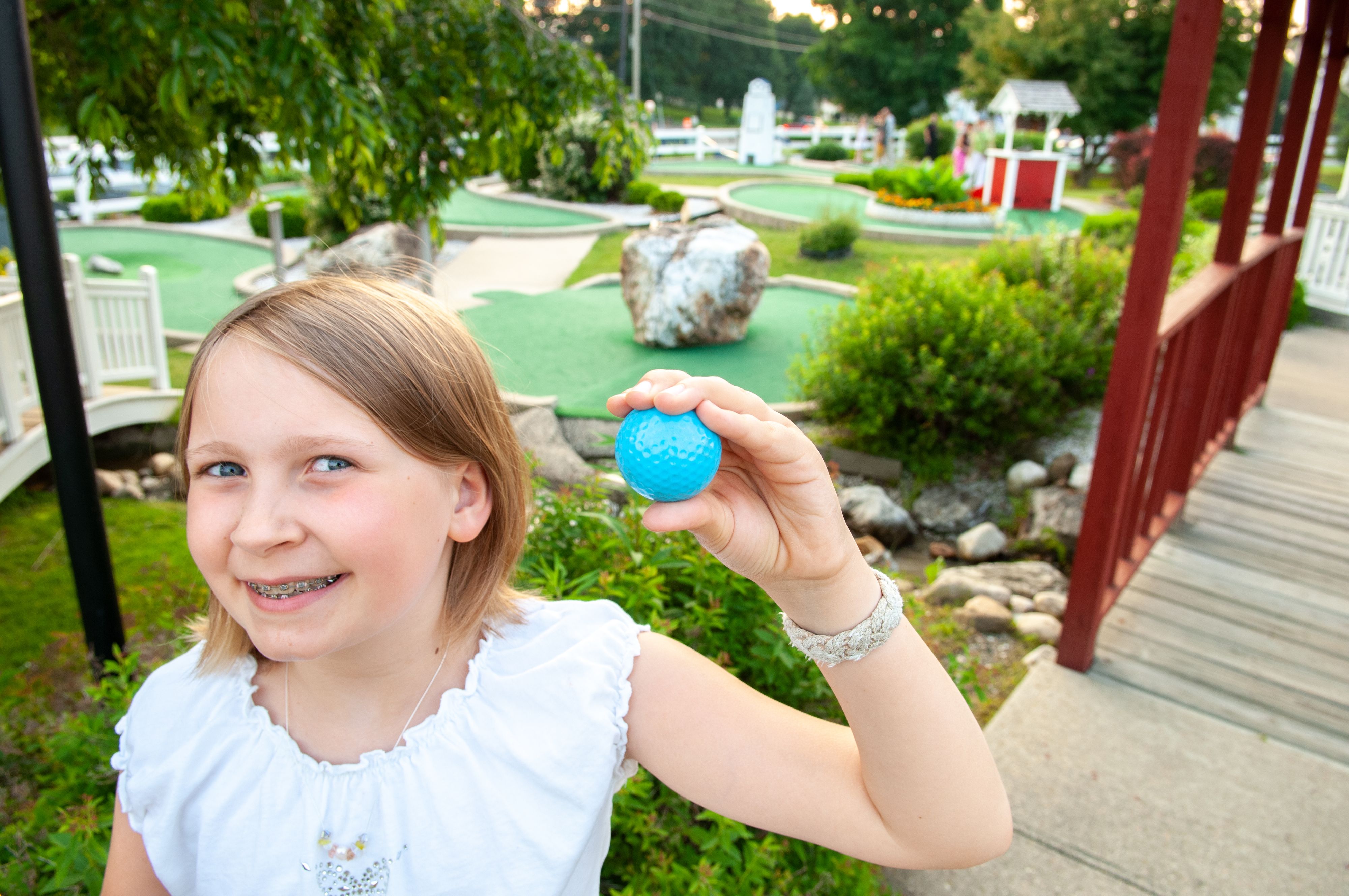 Girl in braces smiles and holds golf ball at mini golf course