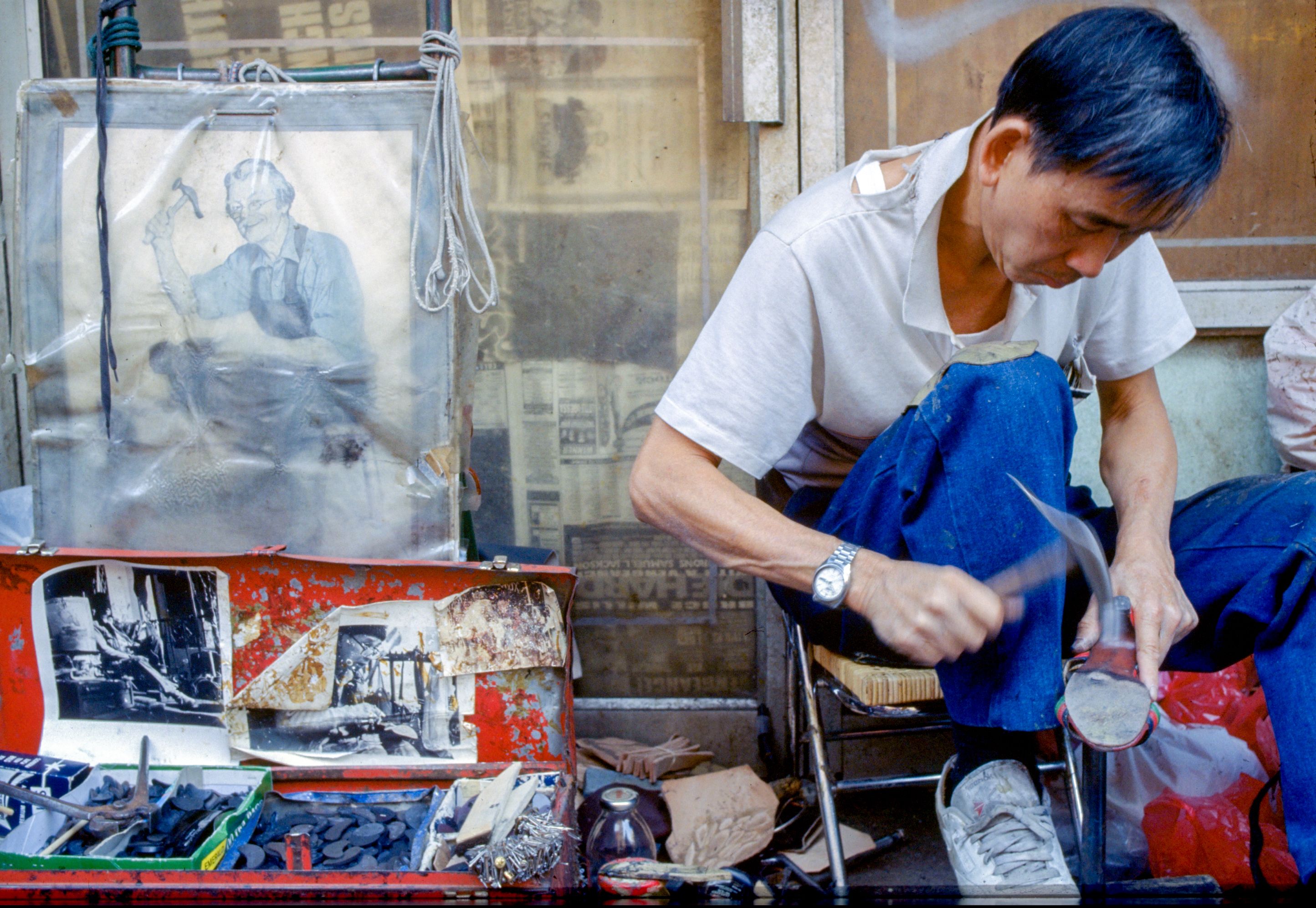NYC street cobbler works on boot repair with tools and vintage cobbler print