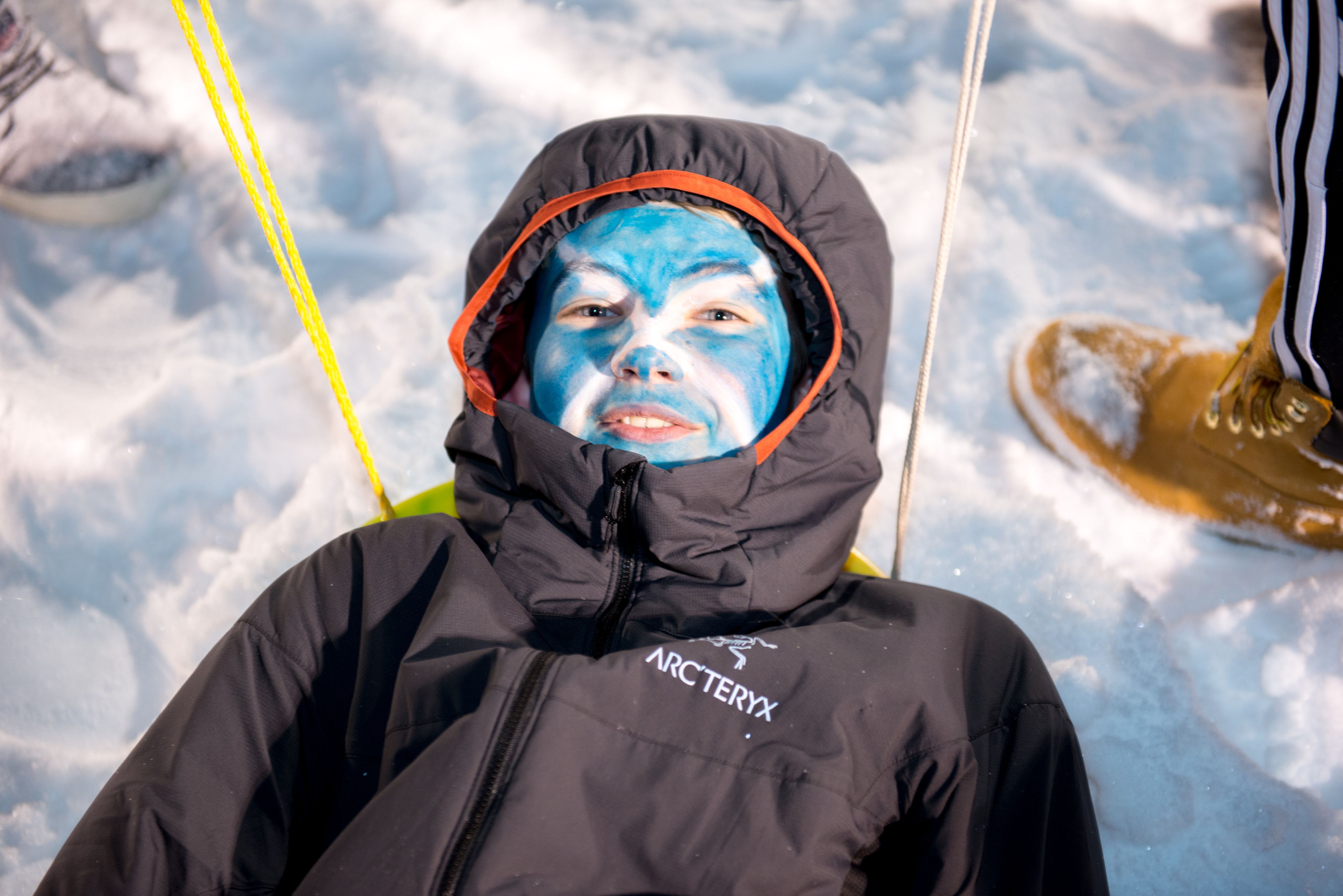 Young woman with blue painted face lying in sled in snow