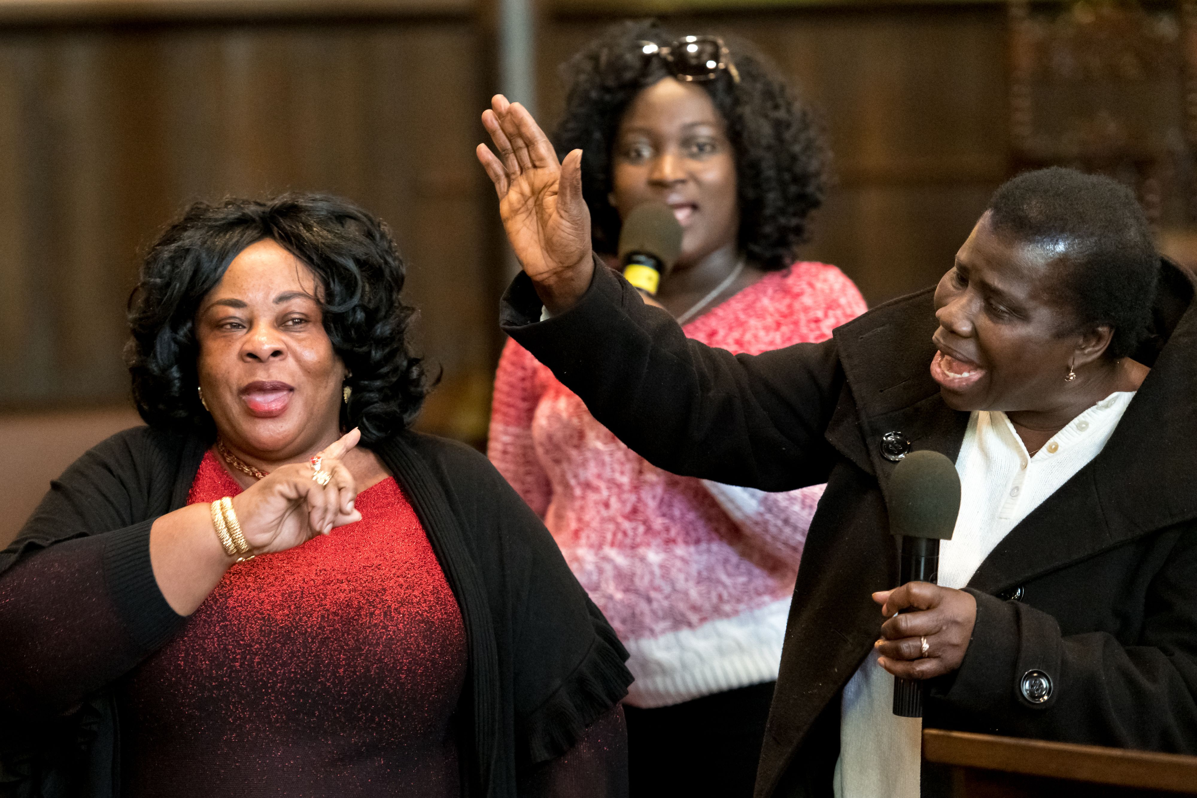 Three African American women singing in church with microphone and hand in air