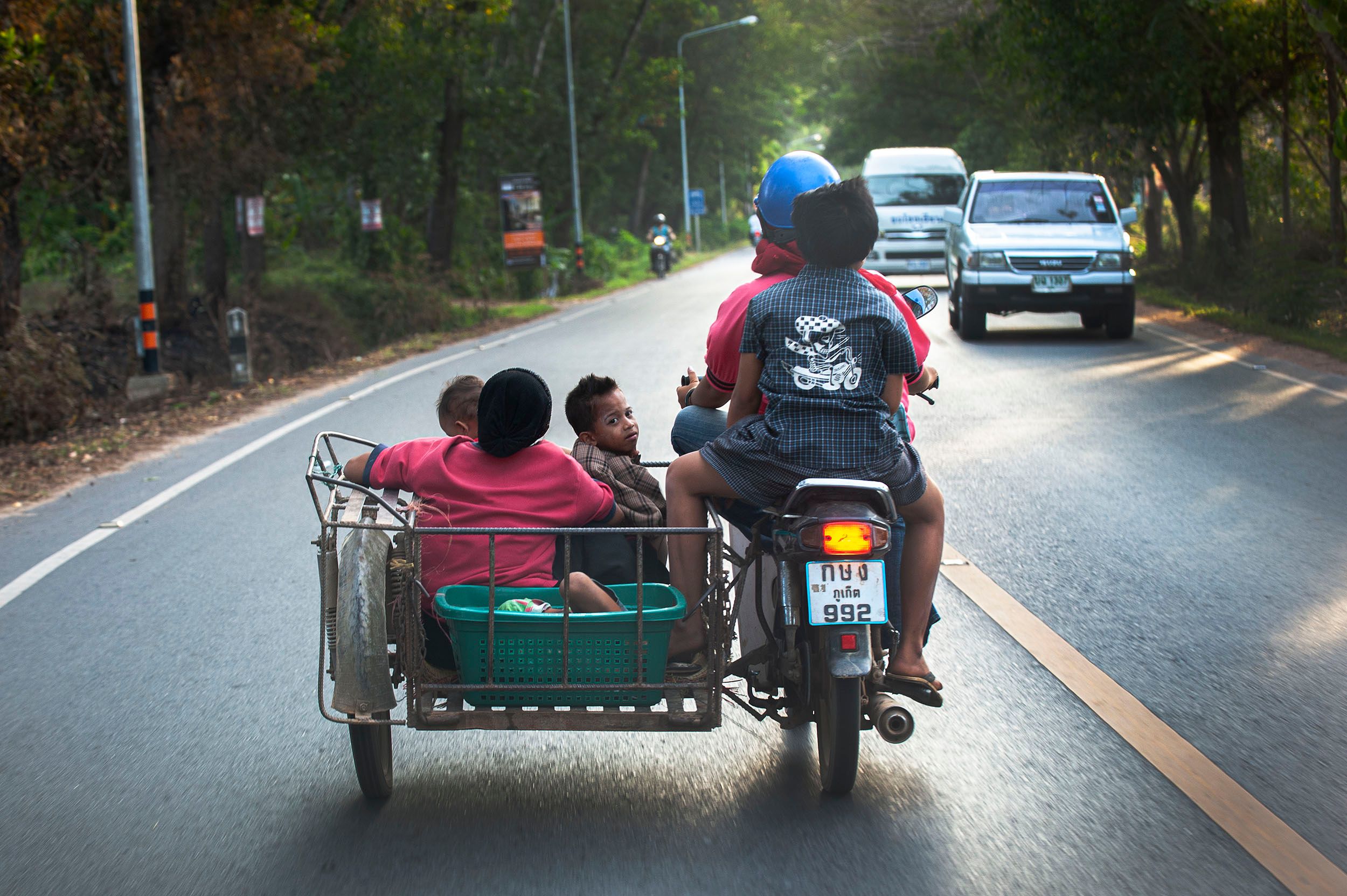 çhild riding in a family motorcycle looks back while everyone else besides the child in the basket, looks forward Looking Back