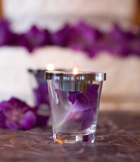 Detail shot of the cake with a purple flower inside the candle holders on the cake table.