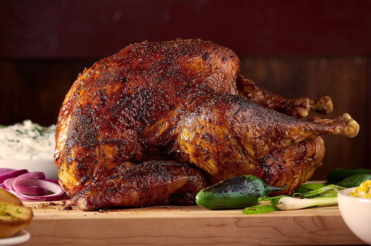 Bone Daddy's whole smoked turkey with a dark pepper rub on a maple board with charred jalapeños and grilled scallions