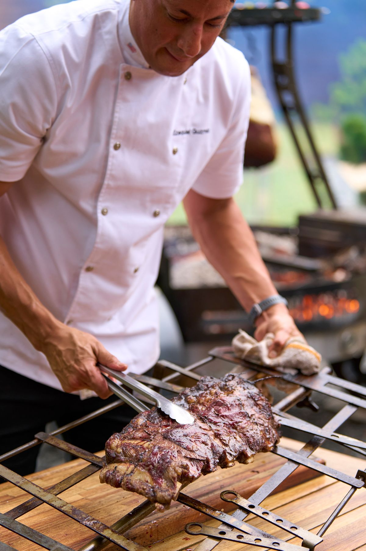 Chef turning a thick Rosewood Wagyu steak with tongs on an iron grate over glowing coals