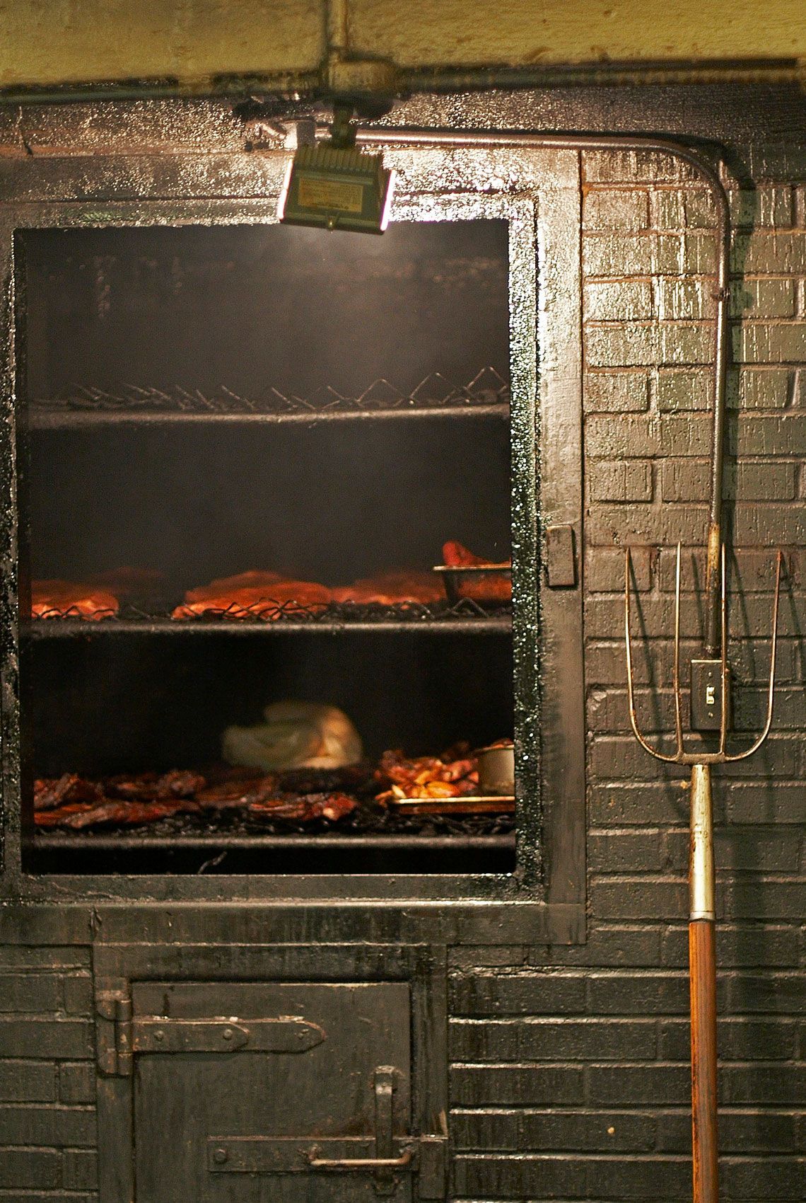 Open brick pit at CT's loaded with ribs and smoked meats, a long-handled fork hanging on the blackened wall beside it