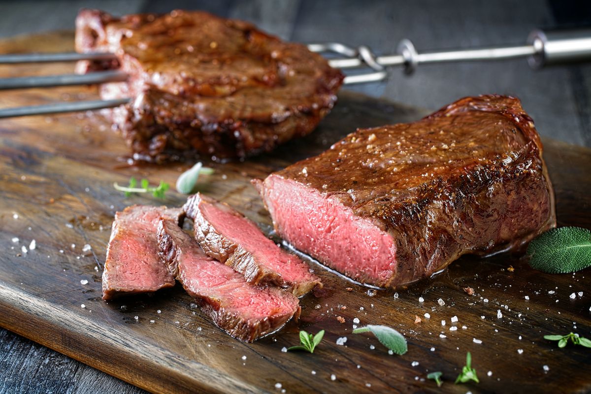 Fogo de Chão steak sliced on a dark wood board with flaked salt, sage, and churrasco skewers behind
