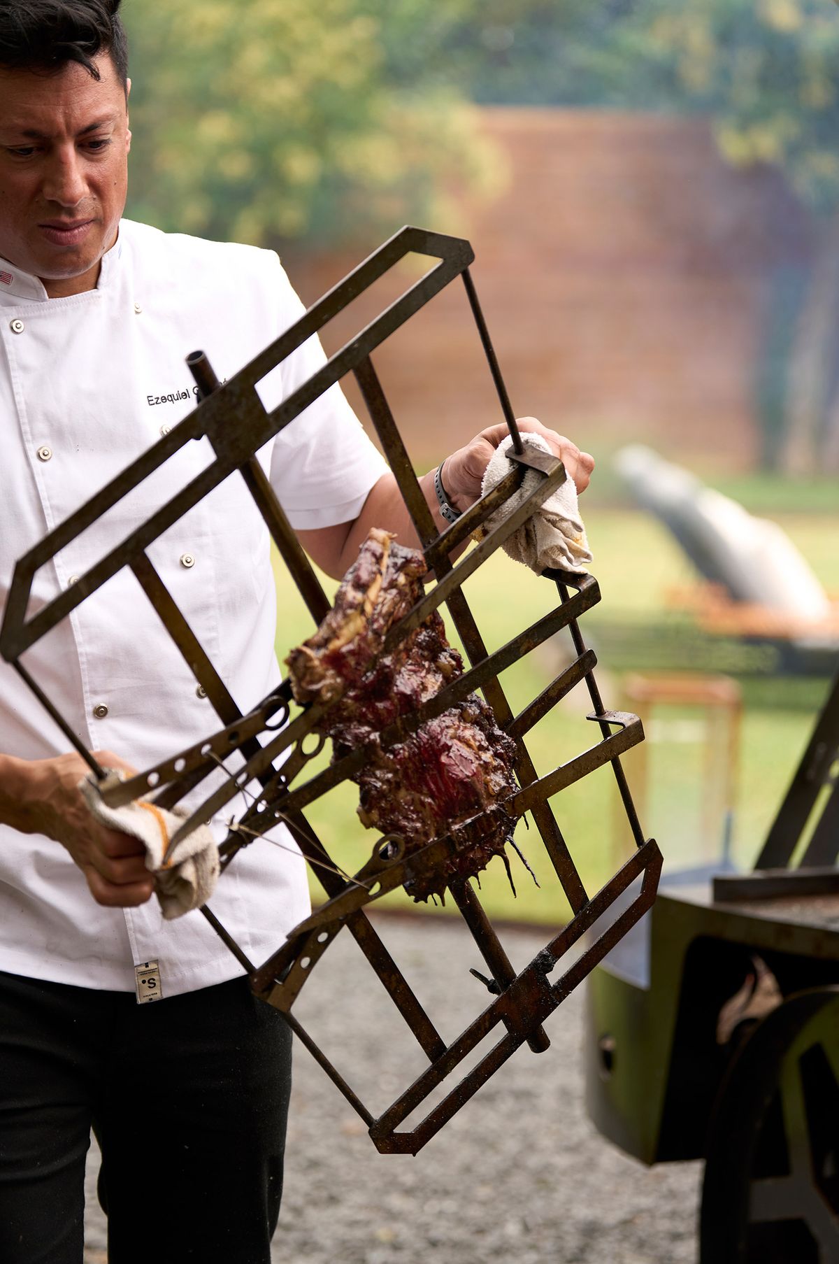 Chef lifting a hinged iron grill basket holding a cooked Rosewood Wagyu cut away from the fire