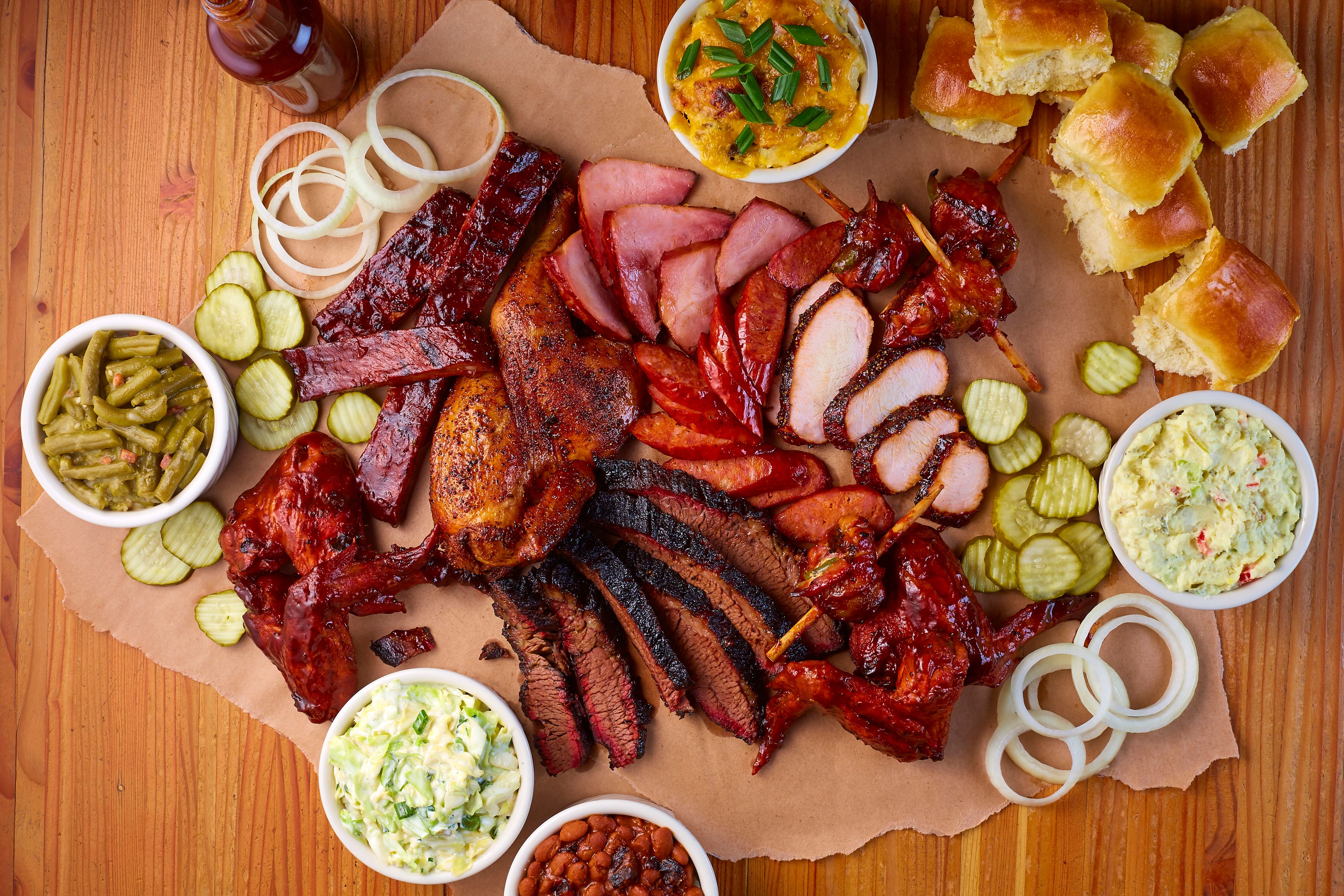 Overhead Bone Daddy's barbecue spread with ribs, brisket, smoked chicken, sausage, stuffed jalapeños, and house sides