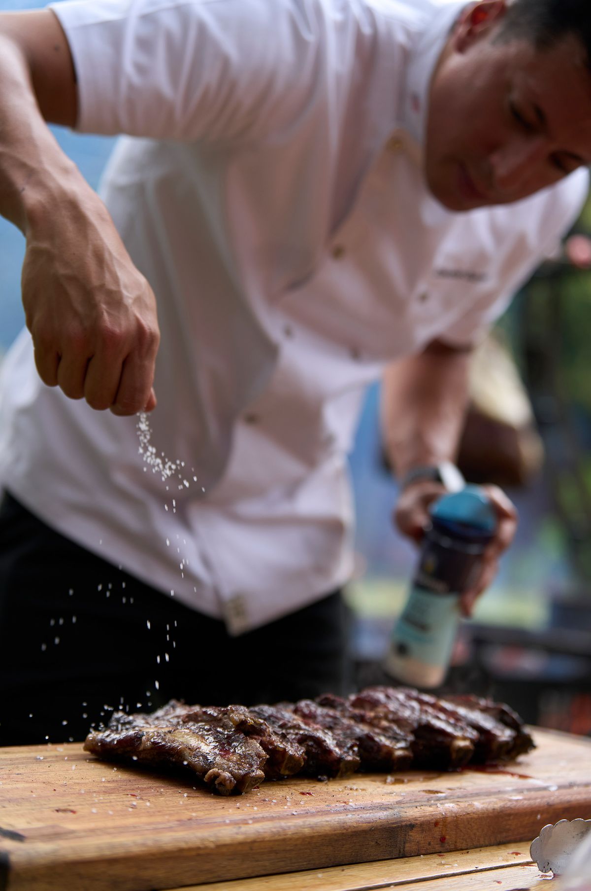 Chef finishing a rack of Rosewood Wagyu ribs with flaked salt on a wood board
