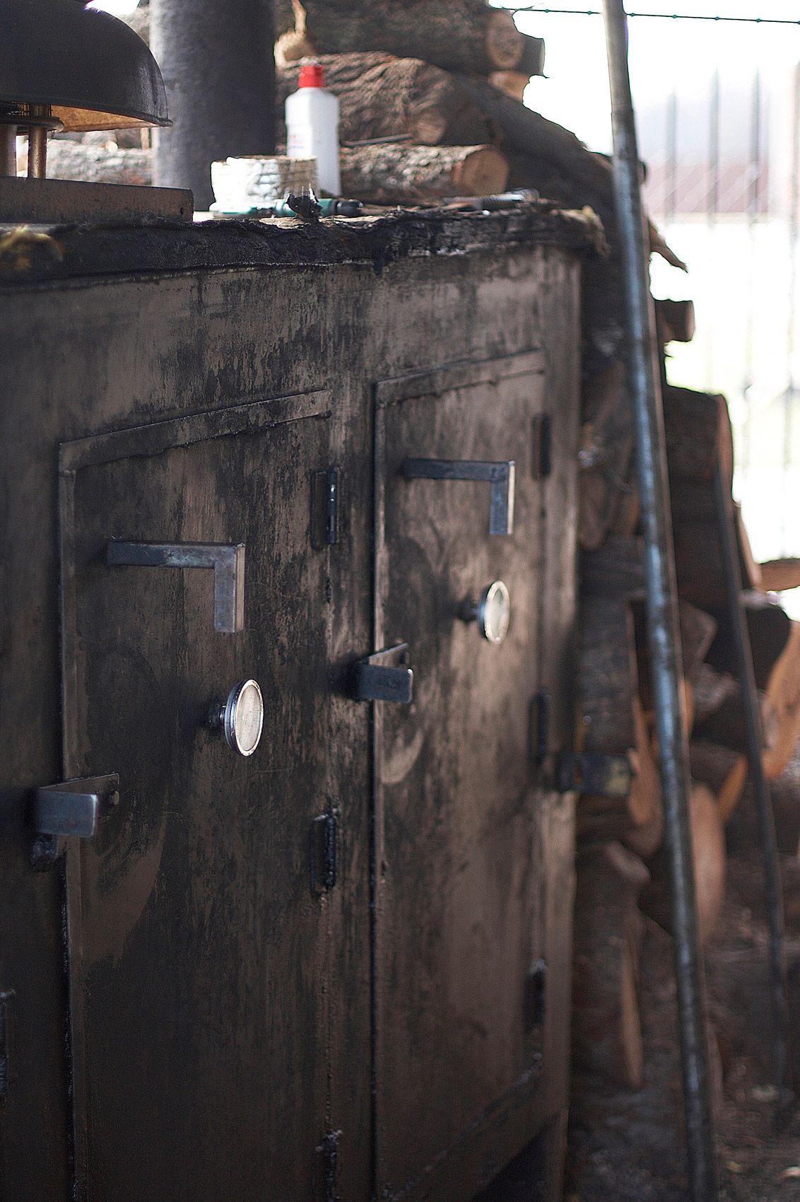 Weathered steel smoker doors blackened from years of service at Off the Bone Barbeque in Dallas, split logs stacked alongside