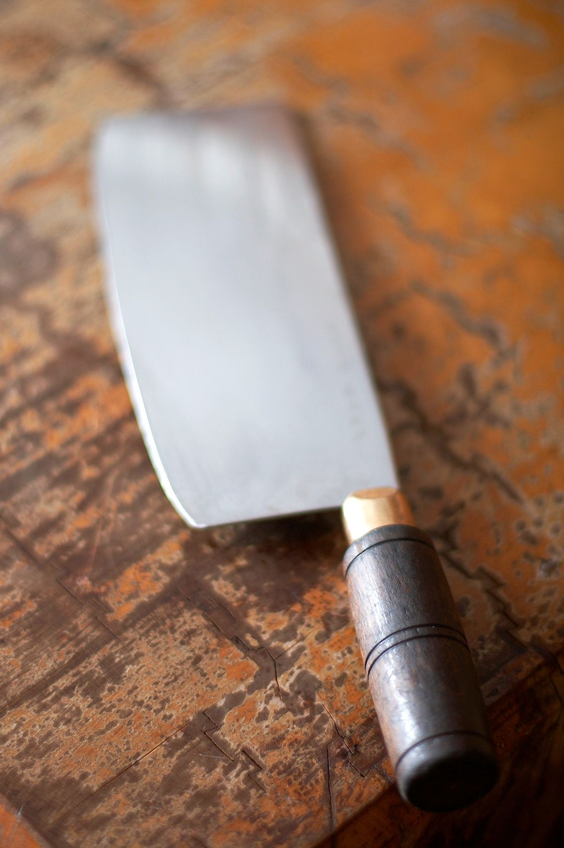 Chinese cleaver with a wood and brass handle resting on a scarred butcher block at Baker's Ribs, shot in shallow focus